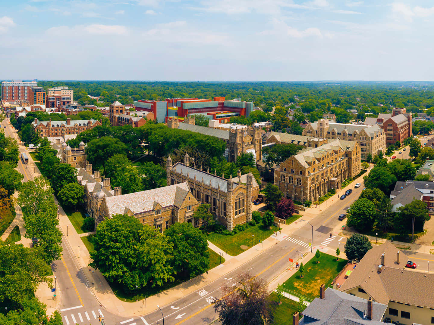 Michigan 桌布 壁紙 — 歷史悠久的大學校園鳥瞰圖，擁有石砌建築和茂密的綠樹，在明亮的藍天下。