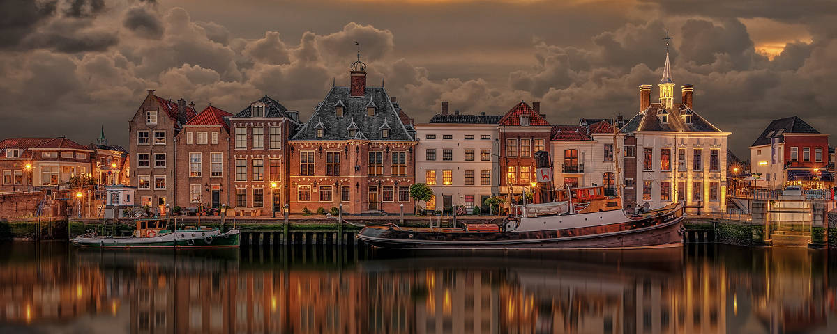 Netherlands 桌布 壁紙 — 歷史悠久的荷蘭運河房屋在黃昏時溫暖地發光，它們的倒影在平靜的水面上閃爍，天空中有戲劇性的雲彩。