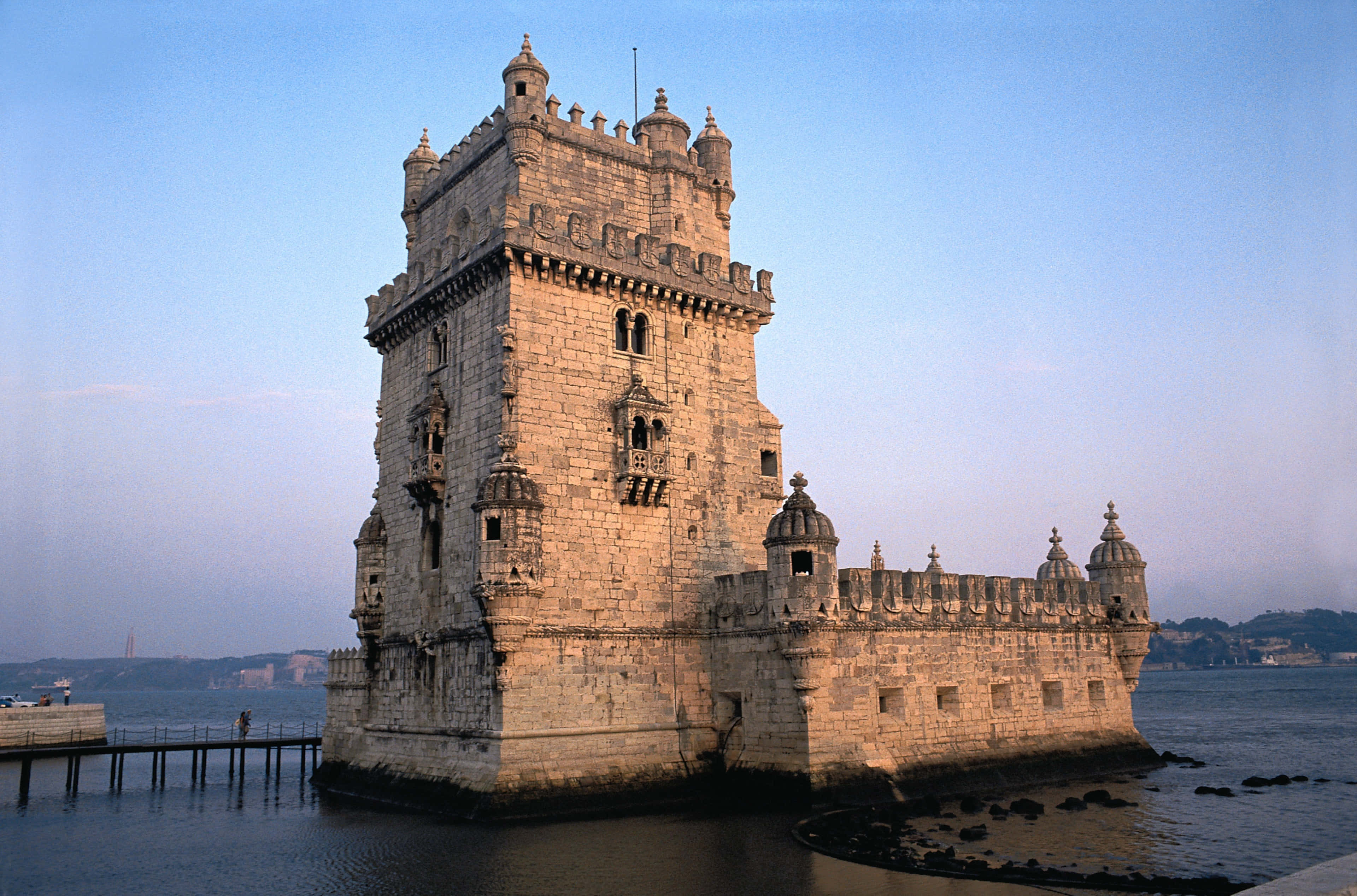 Portugal 桌布 壁紙 — 歷史悠久的貝倫塔在日落時分雄偉地矗立在水面上，溫暖的金色光芒照亮了它的石牆和塔樓。