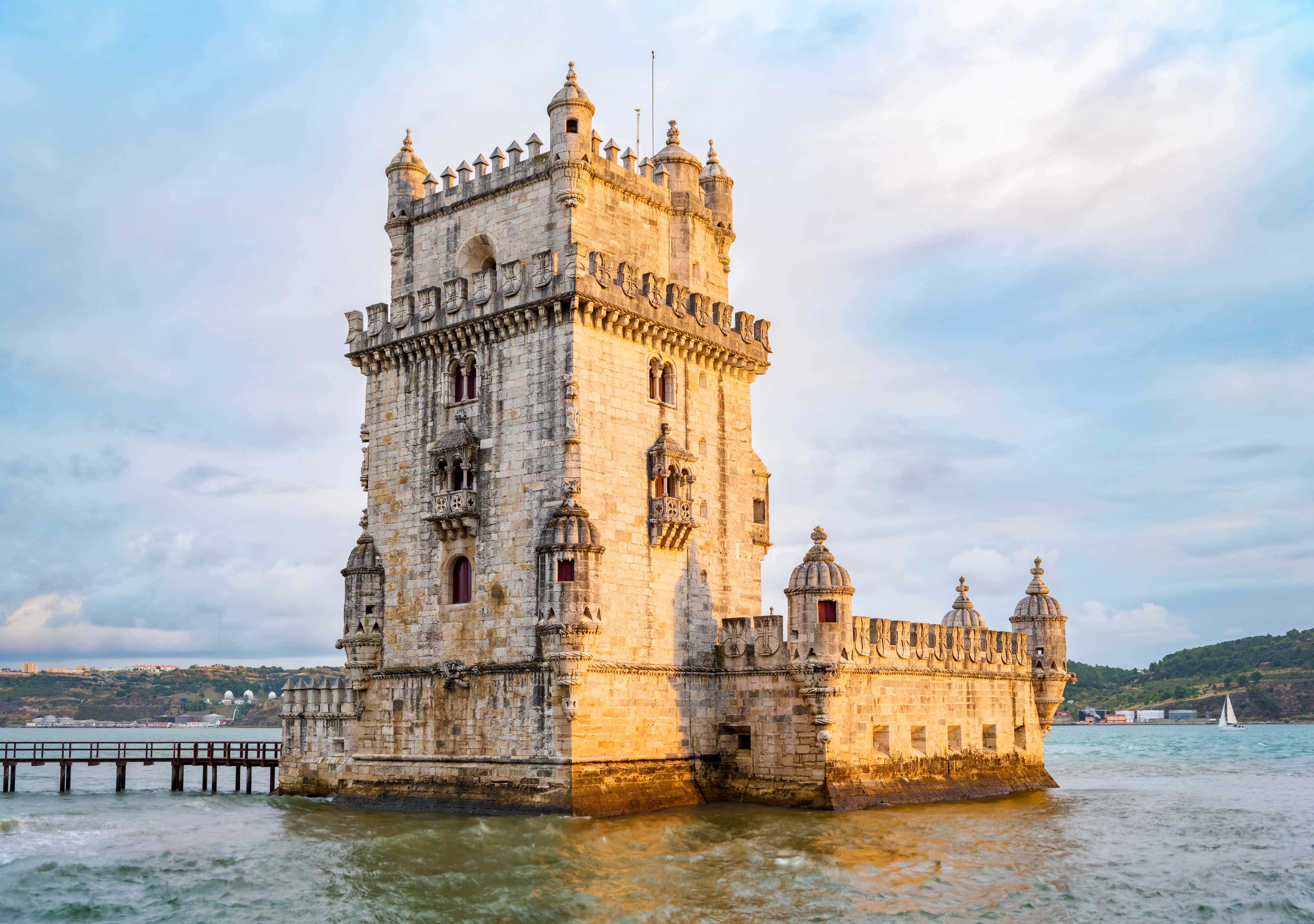 Portugal 桌布 壁紙 — 歷史悠久的貝倫塔在日落時分雄偉地矗立在塔霍河中，溫暖的金色光芒照亮了它的石牆和周圍的水域。
