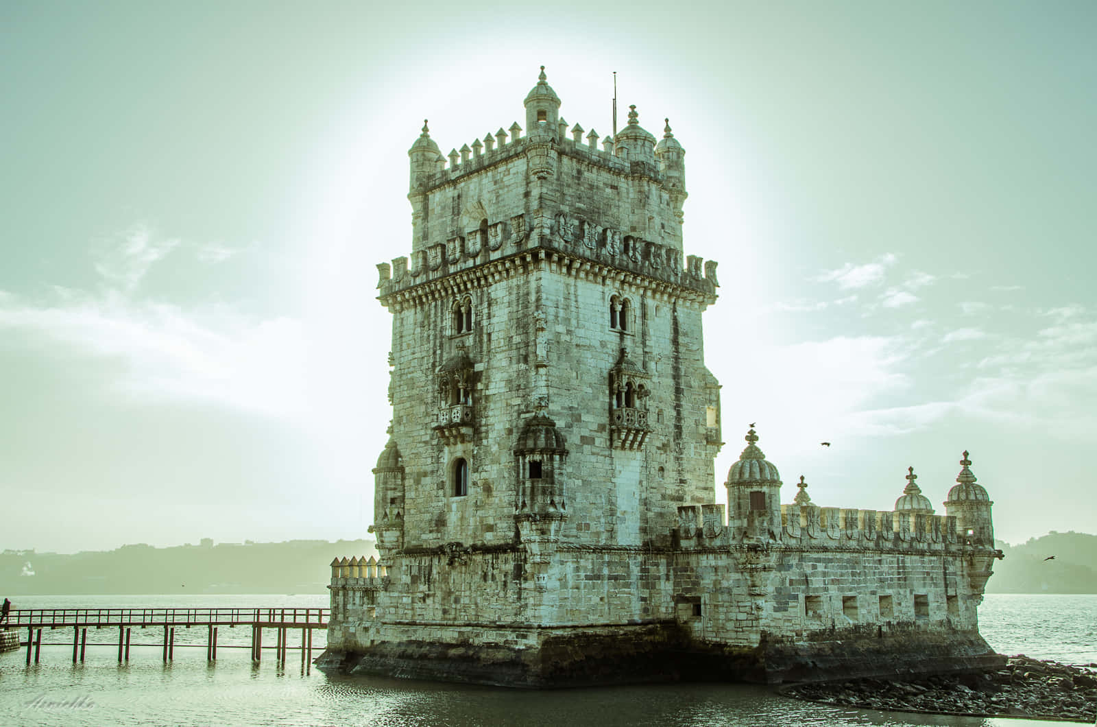 Portugal 桌布 壁紙 — 歷史悠久的貝倫塔在柔和朦朧的天空下雄偉地矗立在水面上，一座木製碼頭向它延伸。