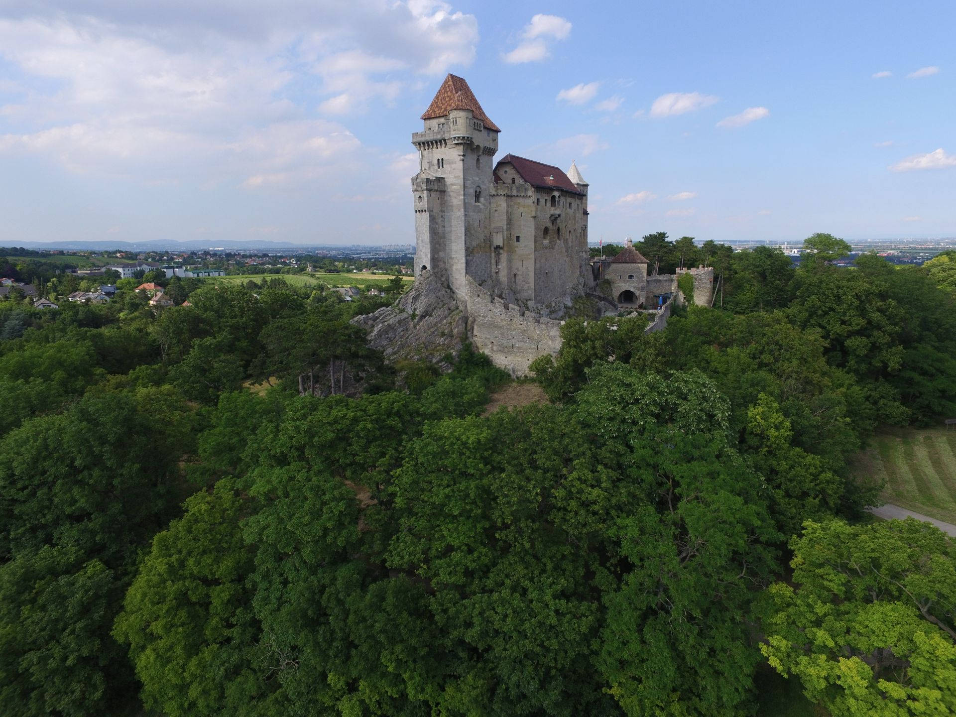 Liechtenstein 桌布 壁紙 — 歷史石城堡的鳥瞰圖，坐落於岩石山丘上，周圍是茂密的綠色森林，天空部分多雲。