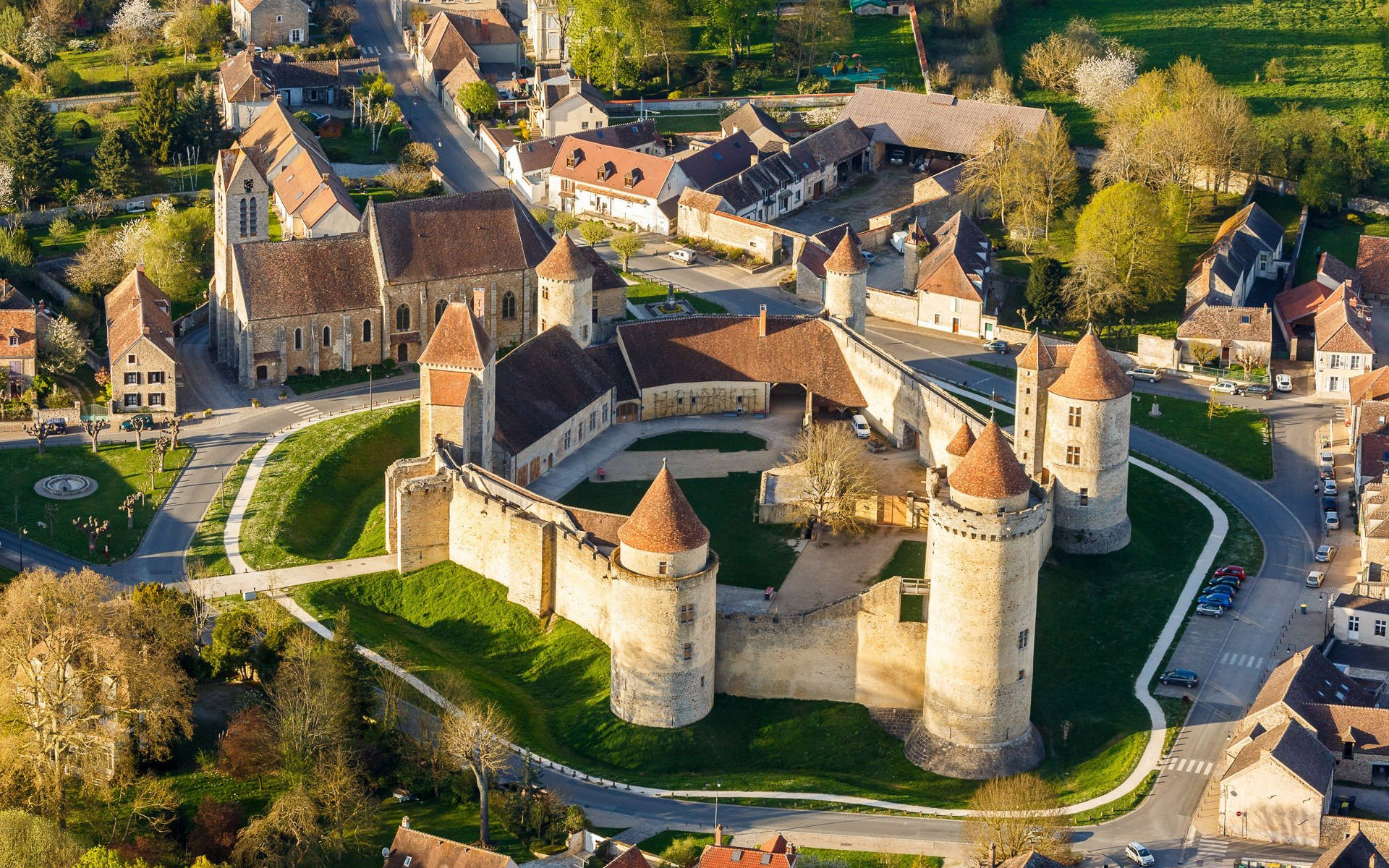 France 桌布 壁紙 — 歷史石城堡的鳥瞰圖，擁有圓錐形屋頂的塔樓，周圍環繞著古色古香的村莊，村莊有紅瓦屋頂和蜿蜒的道路。