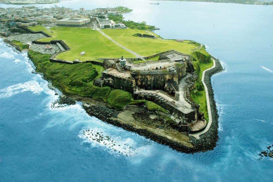 島嶼 桌布 壁紙 — 歷史石堡壘坐落在鬱蔥綠色半島上，被深藍色海洋波浪環繞的鳥瞰圖。