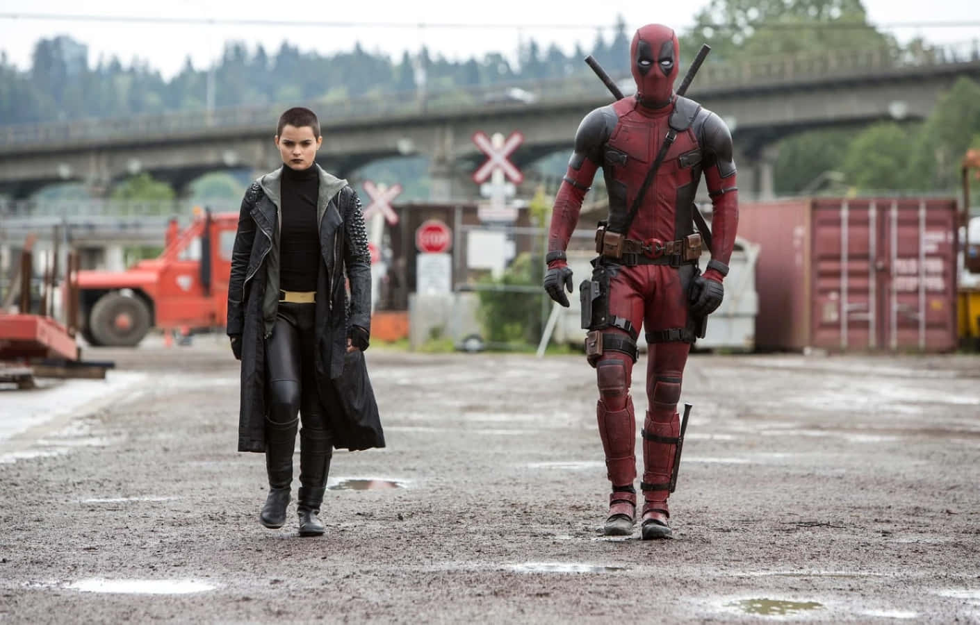 Negasonic Teenage Warhead 桌布 壁紙 — 死侍和多米諾在陰天之下自信地走過濕漉漉的工業場地。