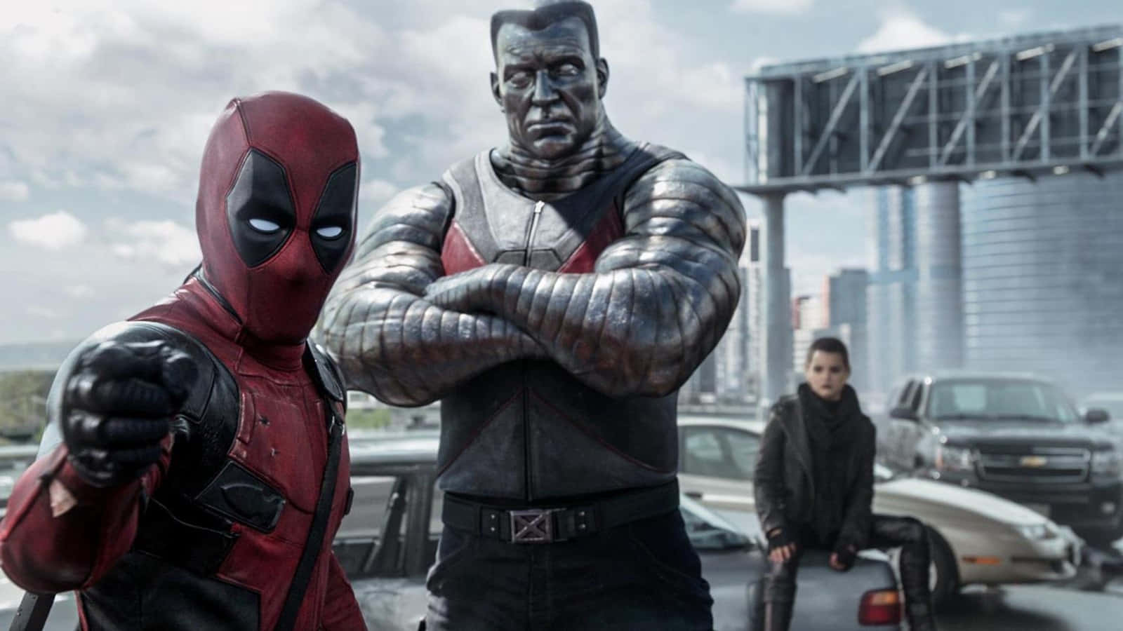 Deadpool And Colossus 桌布 壁紙 — 死侍和鋼人在多雲天空下，於一輛汽車和遠處橋樑的混亂城市街道上挑釁地站立。