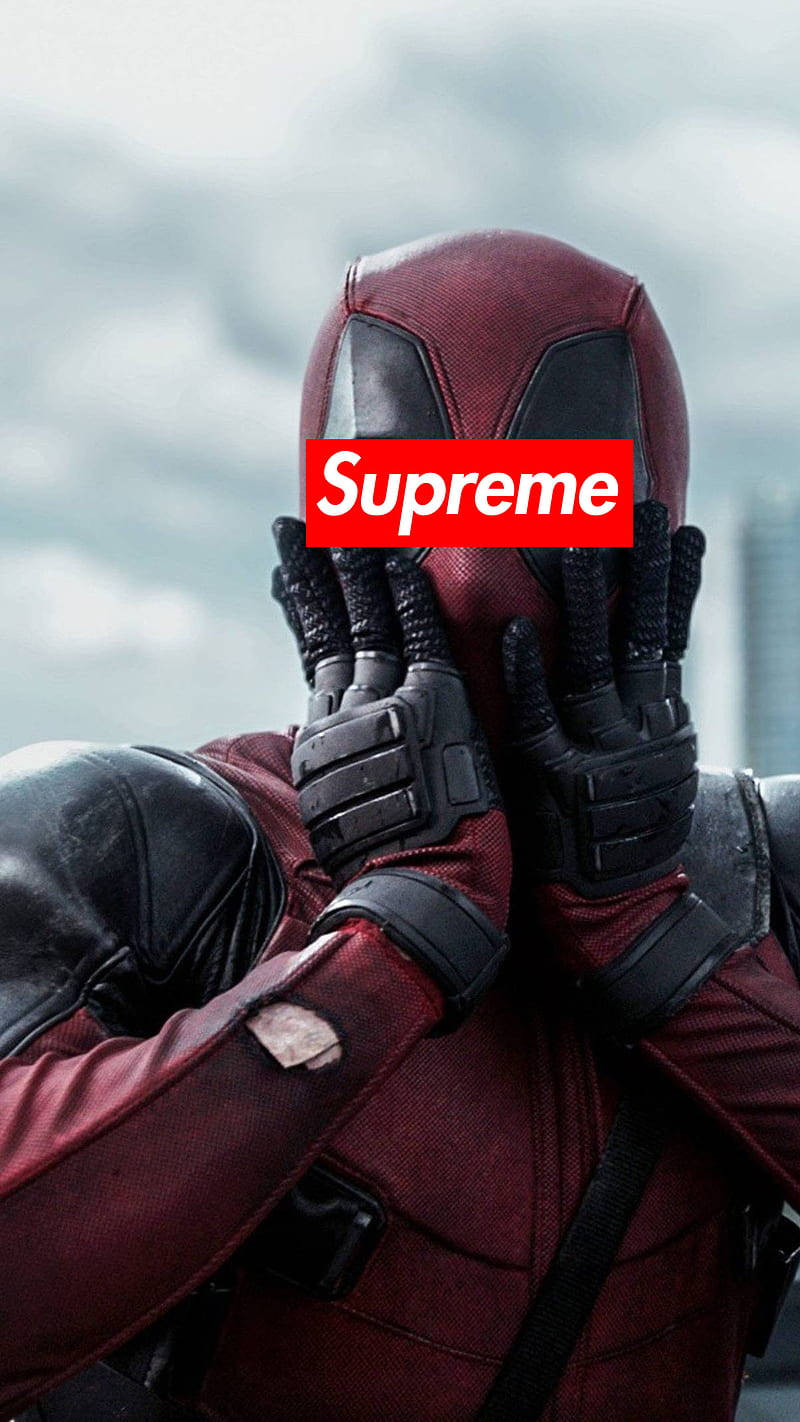 superhero supreme 桌布 壁紙 — 死侍穿著紅黑戰衣，雙手遮臉，露出紅色Supreme標誌，背景是多雲的天空。