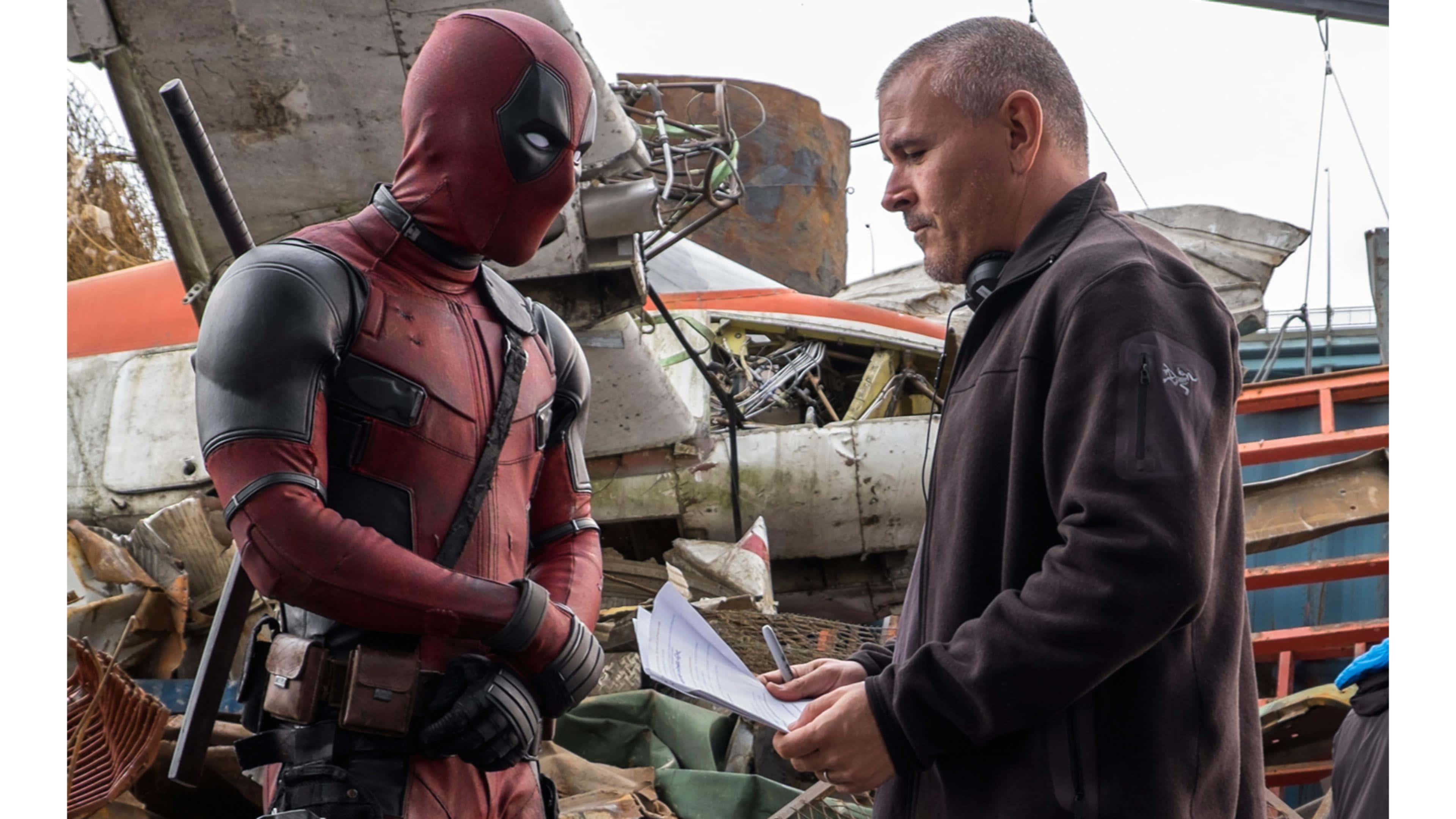 Deadpool 2 桌布 壁紙 — 死侍身穿紅色戰衣，在墜機殘骸中與導演交談。