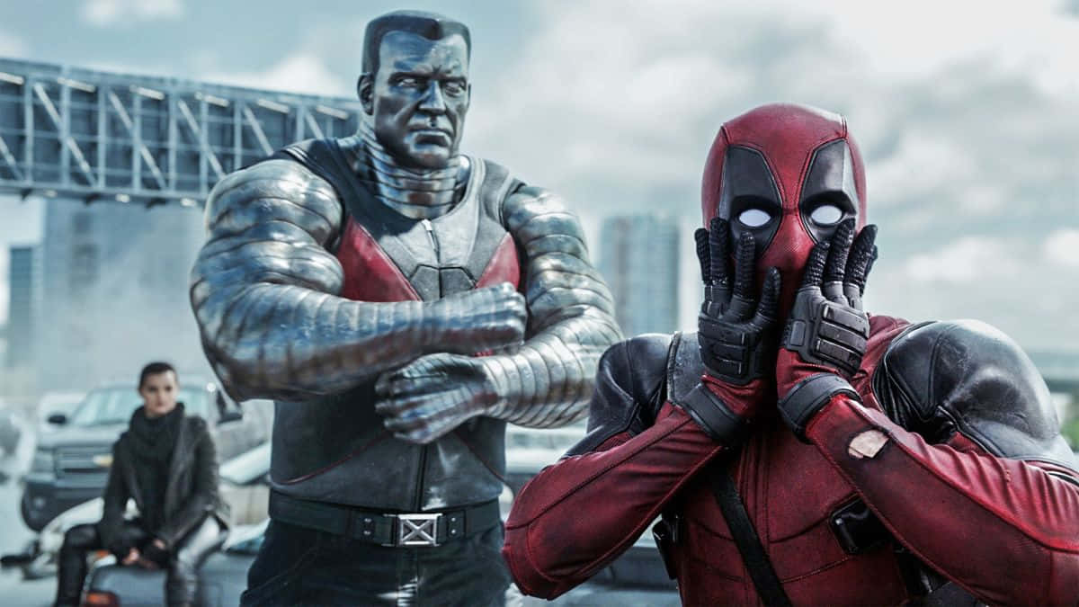 Deadpool And Colossus 桌布 壁紙 — 死侍身穿紅色戰衣，戴手套的雙手遮臉，而機堡身穿金屬裝甲，雙臂交叉站立於城市環境中。