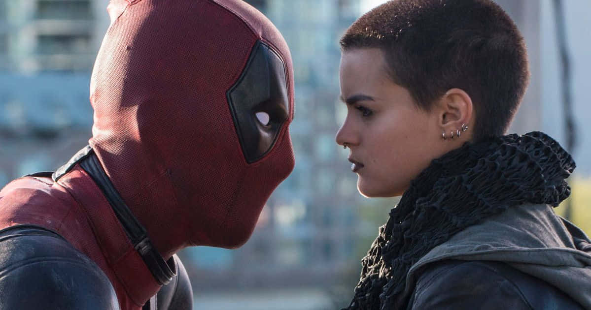 Deadpool And Negasonic Teenage Warhead 桌布 壁紙 — 死侍身穿紅色戰衣，與一位短髮戴黑色圍巾的女子在緊張的城市對峙中對決。