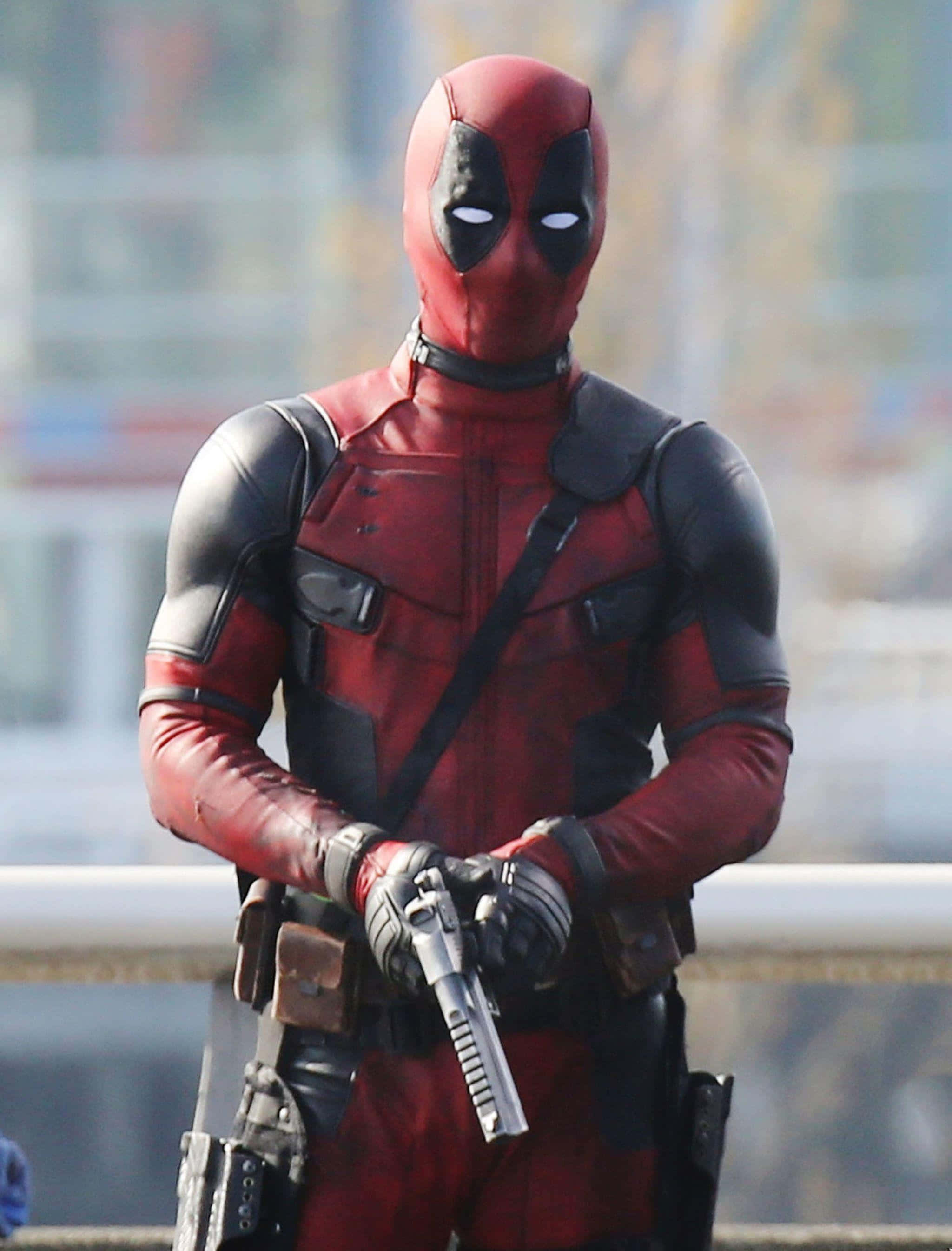 Deadpool 2 桌布 壁紙 — 死侍身穿紅黑戰衣，手持槍械，背景是模糊的城市景觀。