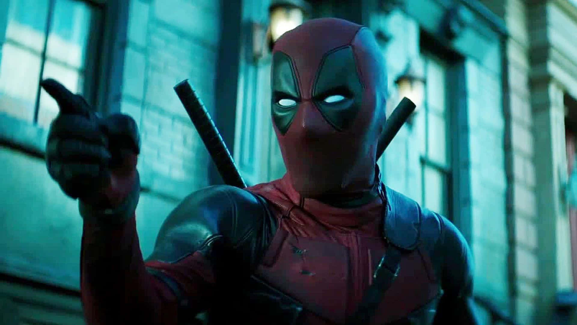 Deadpool 2 桌布 壁紙 — 死侍身穿紅黑戰衣，背負武士刀，在青綠色燈光照耀的都市建築物外牆前指向前方。