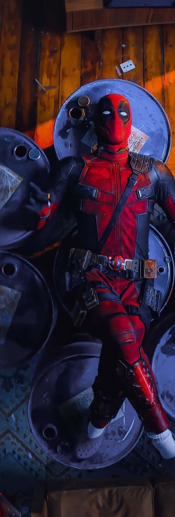 Deadpool Cartoon 桌布 壁紙 — 死侍隨意地躺在堆疊的金屬桶上，身處一個燈光昏暗、帶有溫暖橙色照明的木造房間。