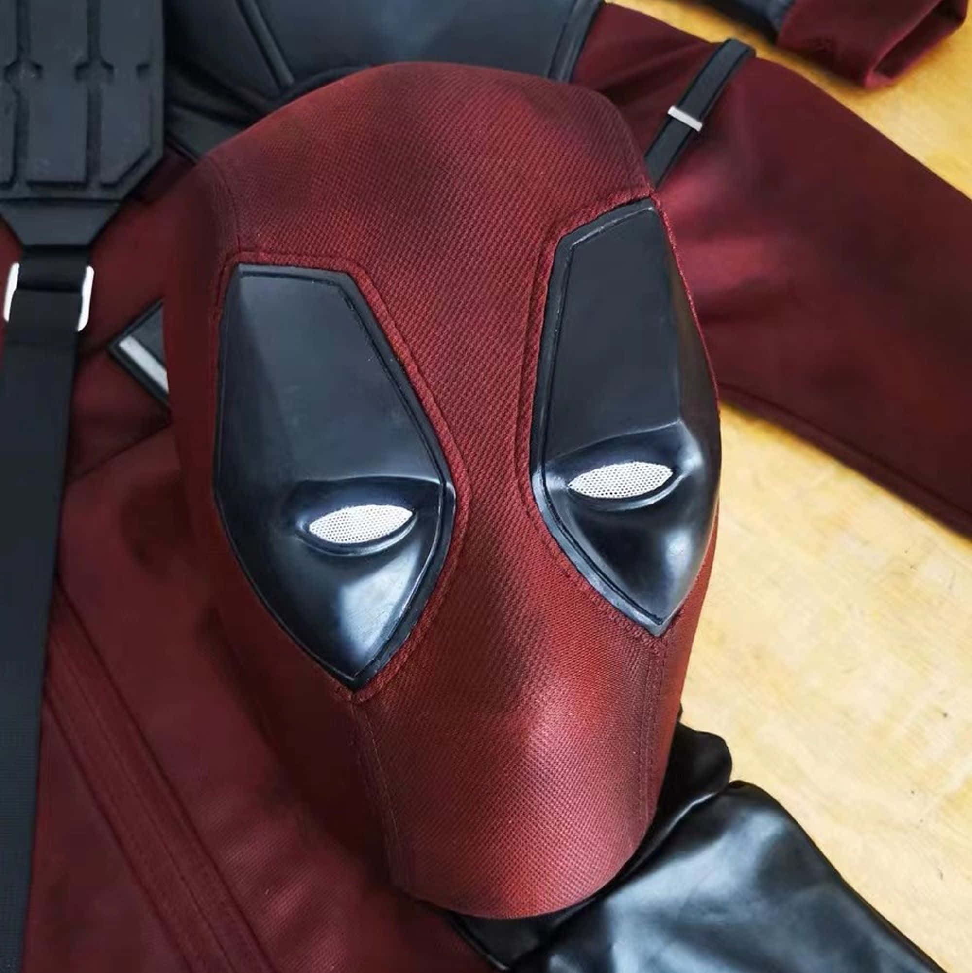 Deadpool Mask 桌布 壁紙 — 死侍面具特寫，紅色布料與黑色眼孔，放在木地板上，旁邊有服裝配件。