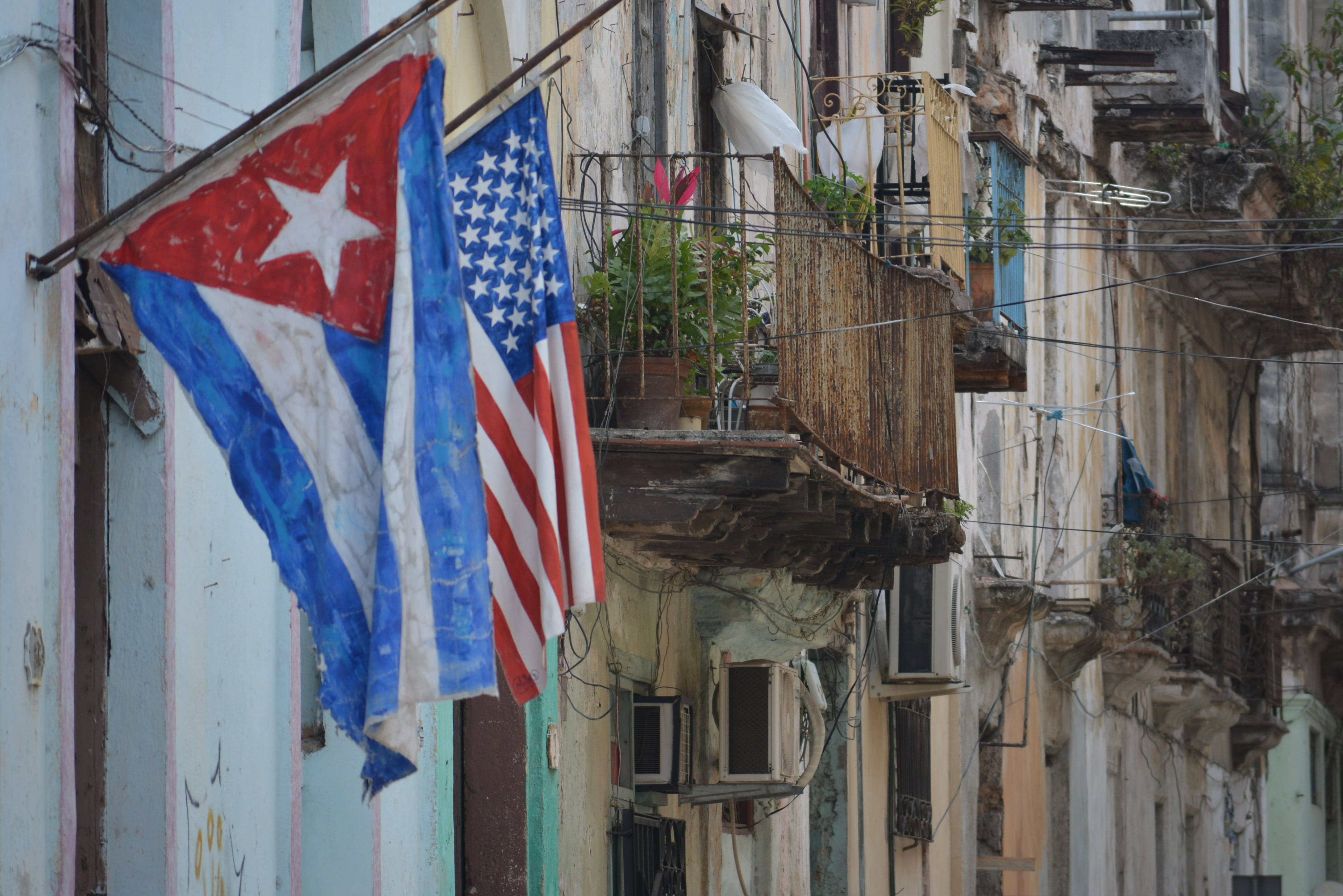 Cuban 桌布 壁紙 — 殘舊的古巴和美國國旗並排掛在風化的殖民建築背景下，有陽台和纏繞的電線。
