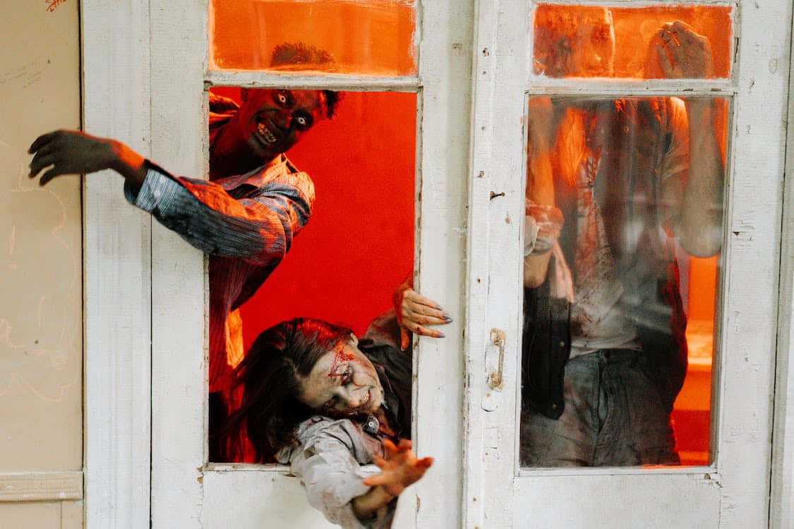 Scary Zombie 桌布 壁紙 — 殭屍滿臉鮮血、衣衫襤褸，在火紅背景下抓撓白色大門。