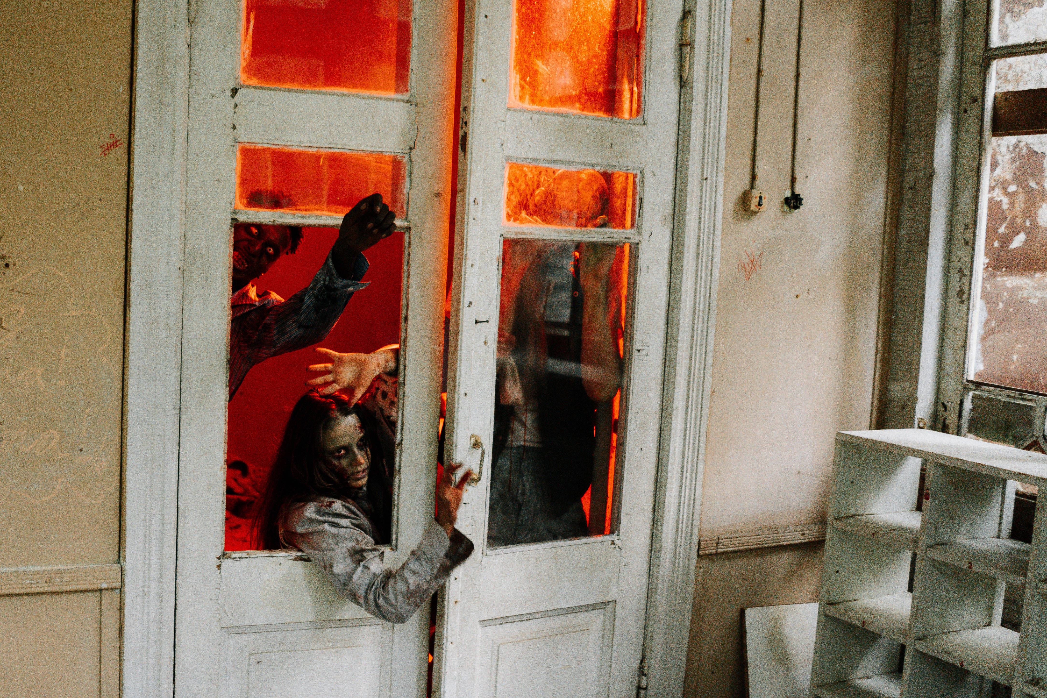 Most Scary 桌布 壁紙 — 殭屍穿過一扇帶有發光紅色玻璃窗的白色門，進入一個破舊的房間。