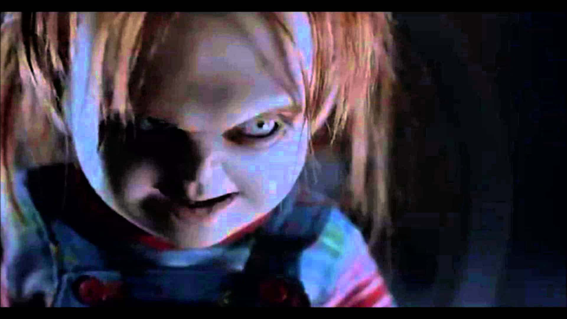 Chucky Doll 桌布 壁紙 — 殺人娃娃Chucky在昏暗燈光下，雙眼發光、露出邪惡笑容的特寫。