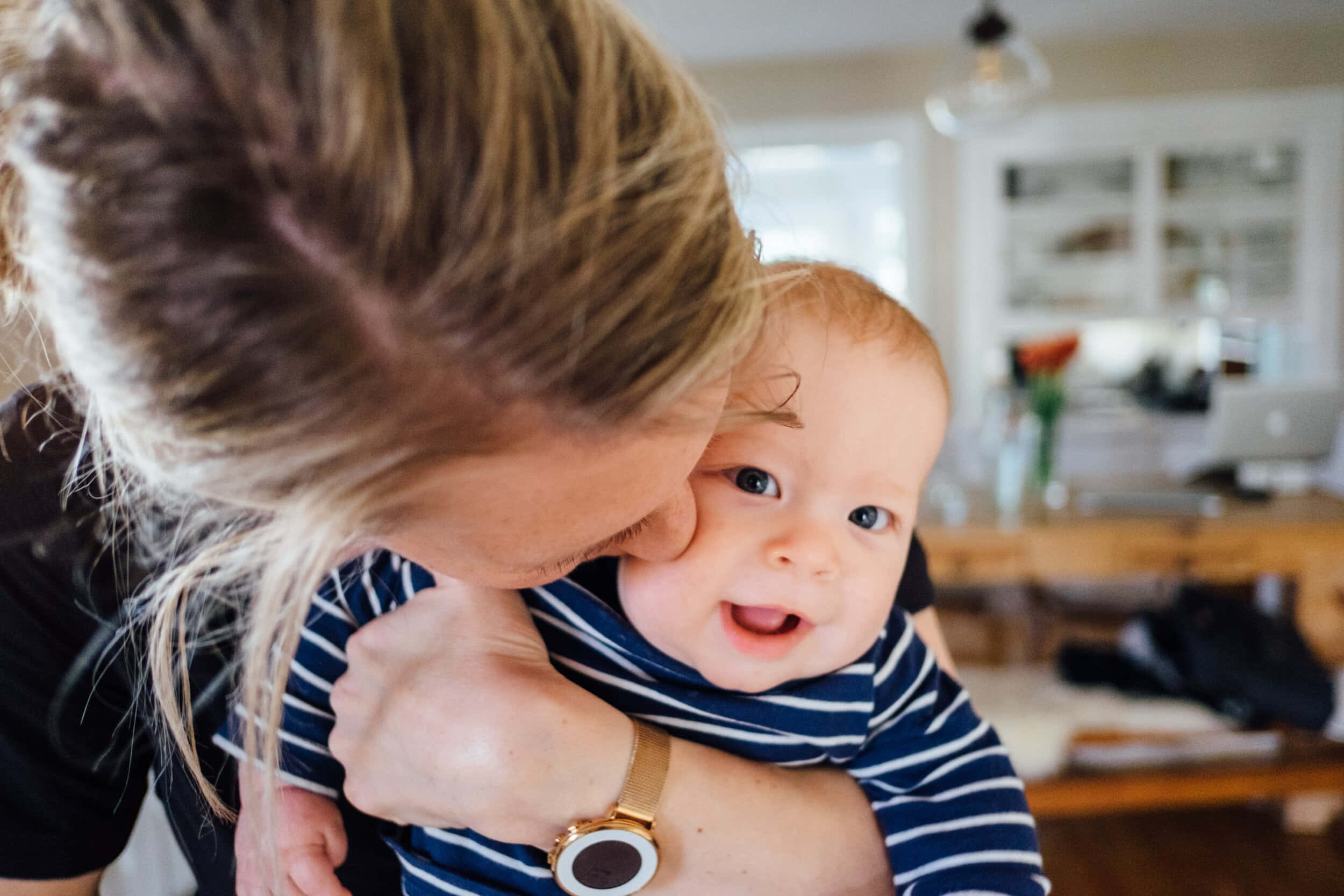 Baby Boy 桌布 壁紙 — 母親在明亮舒適的廚房裡溫柔地親吻微笑的嬰兒的臉頰。