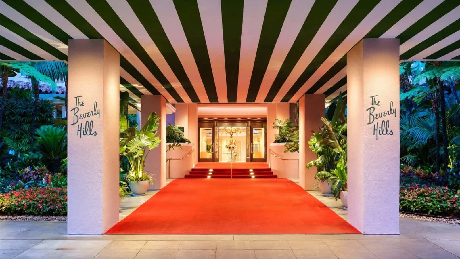 Hotel 桌布 壁紙 — 比佛利山酒店的宏偉入口，以一條大膽的紅地毯為特色，兩旁種滿茂盛的熱帶植物，上方是引人注目的綠色和白色條紋遮篷。