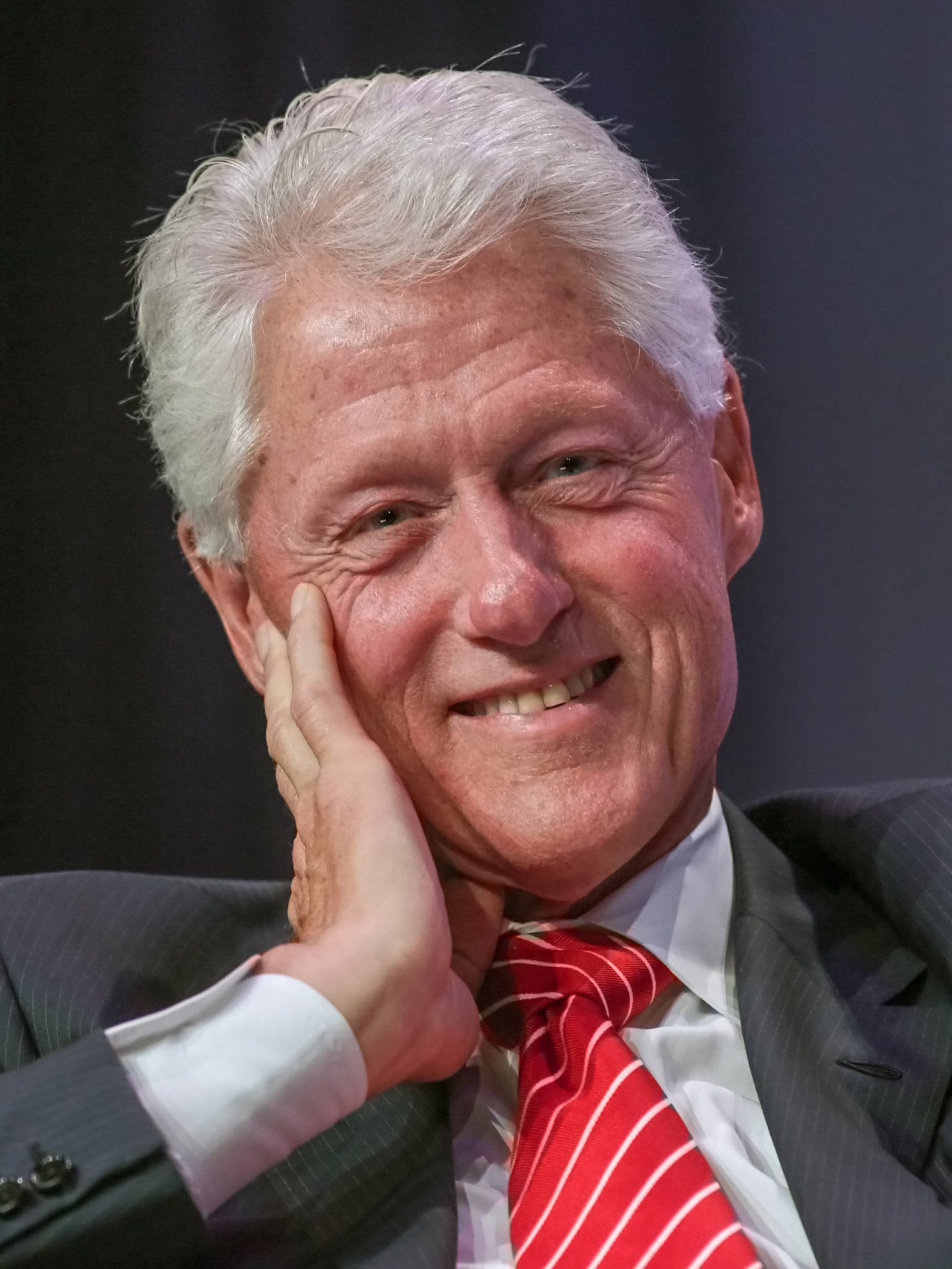 bill clinton 桌布 壁紙 — 比爾·柯林頓的近照，他溫暖地微笑，手放在臉頰上，穿著西裝和紅色條紋領帶。