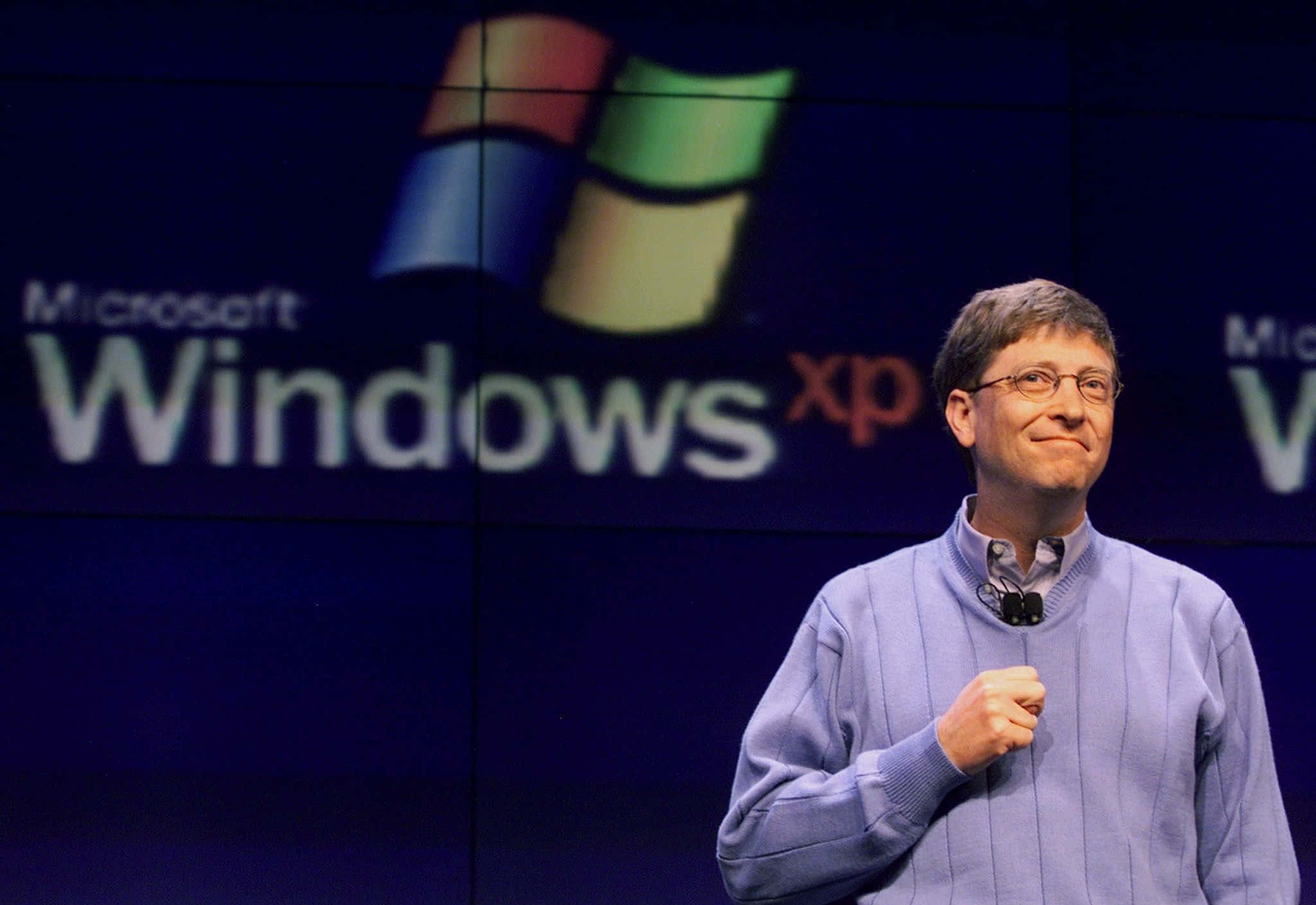 Bill Gates 桌布 壁紙 — 比爾·蓋茲在大型Microsoft Windows XP標誌背景前自信地微笑。