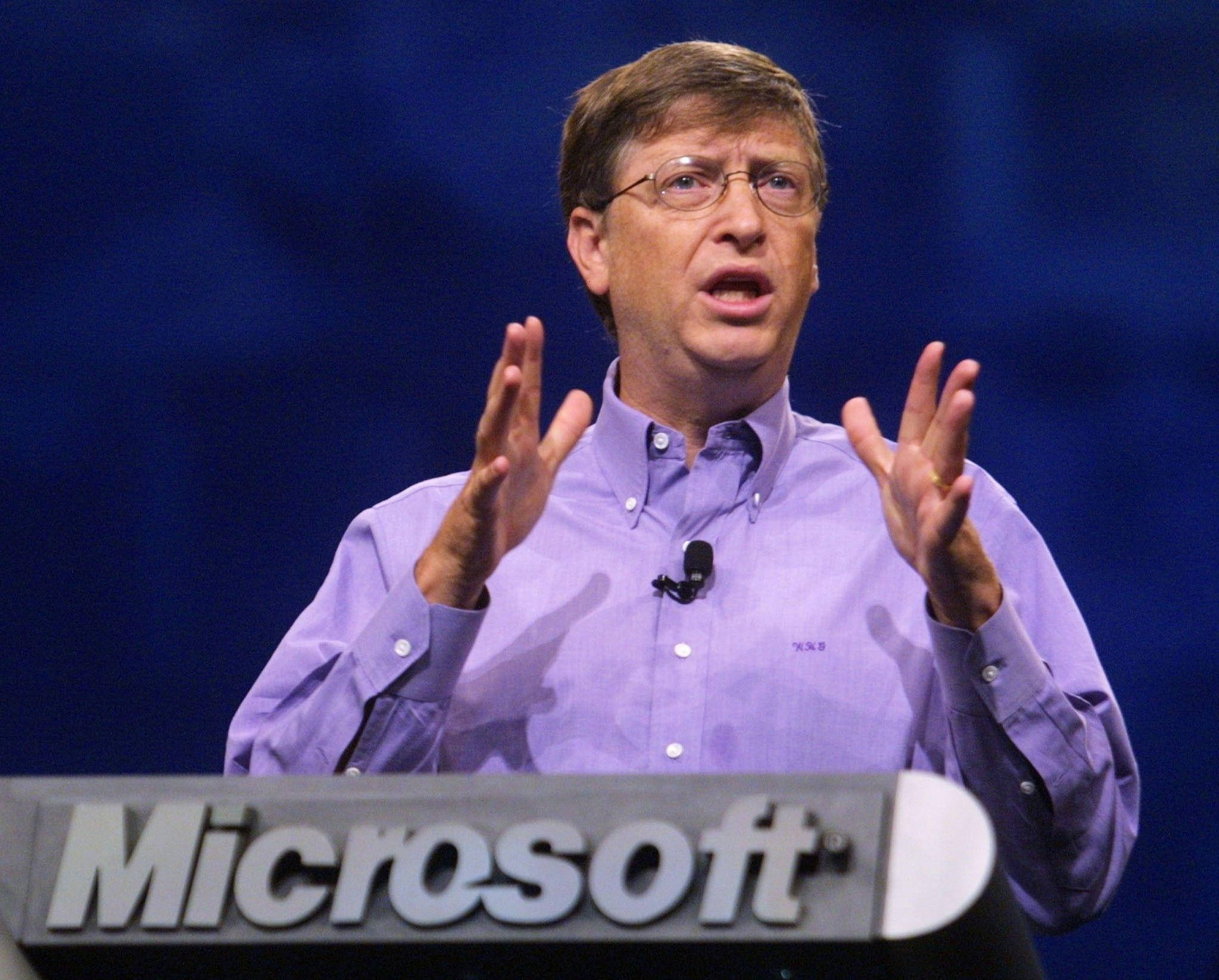 gates 桌布 壁紙 — 比爾·蓋茲在微軟活動中熱情演講，身穿紫色襯衫，背景為深藍色。