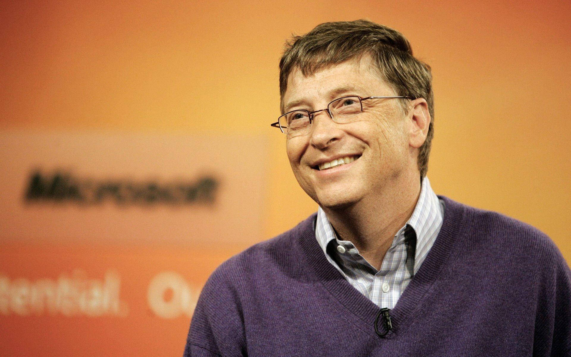 gates 桌布 壁紙 — 比爾·蓋茲穿著紫色毛衣，在橙色微軟品牌背景前溫暖地微笑。