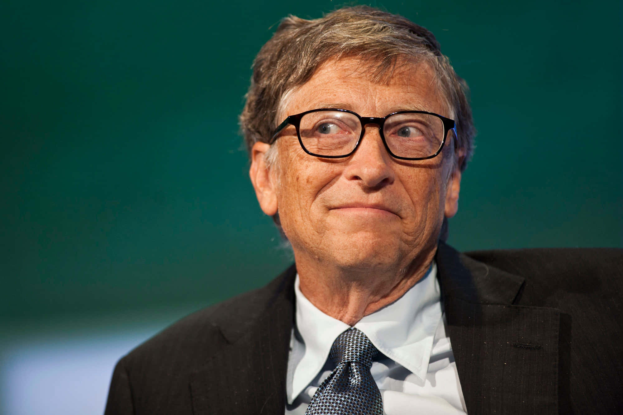 Bill Gates 桌布 壁紙 — 比爾蓋茲的近距離肖像，身穿深色西裝和圖案領帶，背景為青綠色，表情若有所思。