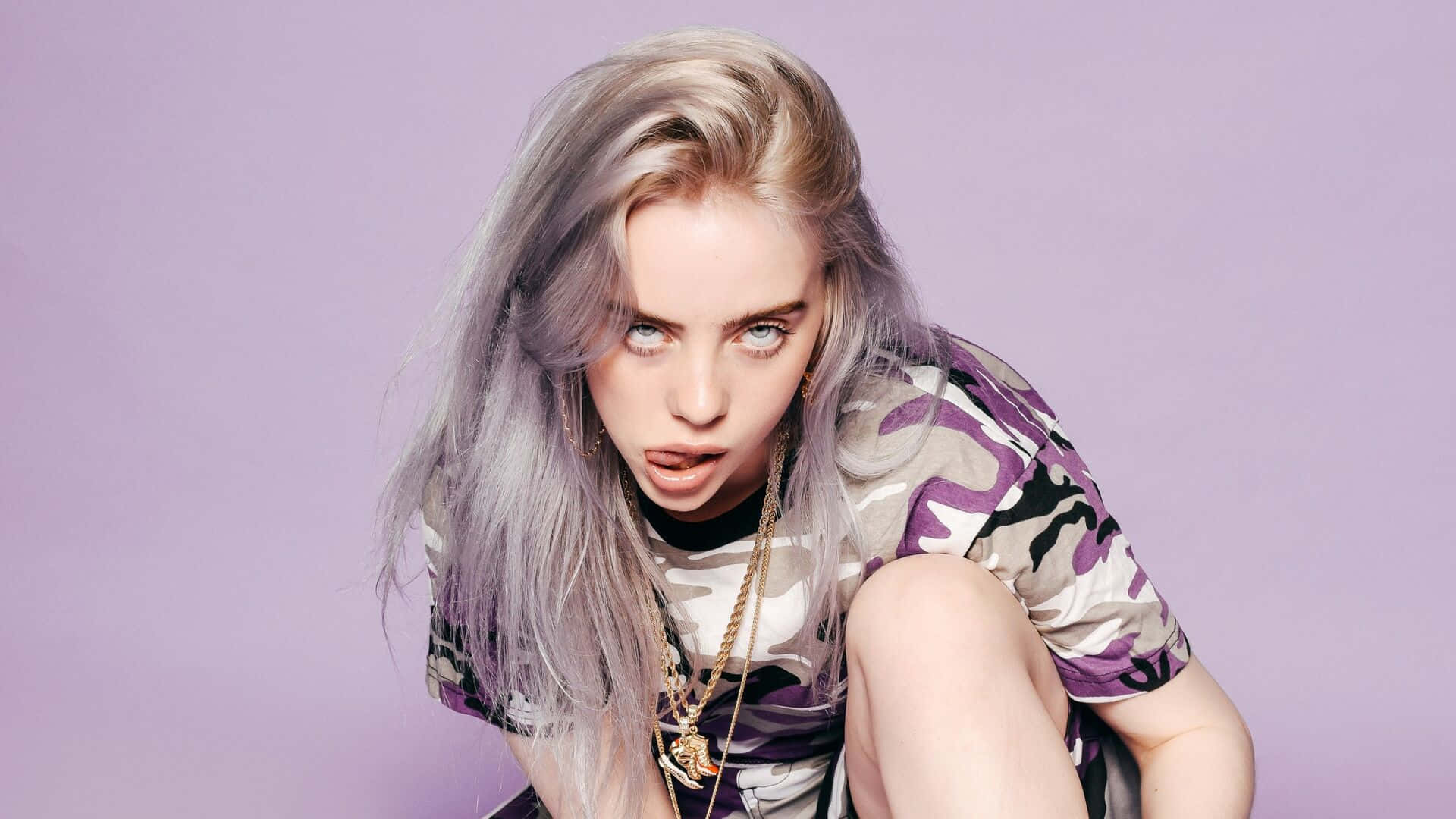 Billie Eilish Laptop 桌布 壁紙 — 比莉·艾利什蹲在薰衣草背景前，身穿迷彩襯衫和金鏈，表情俏皮。