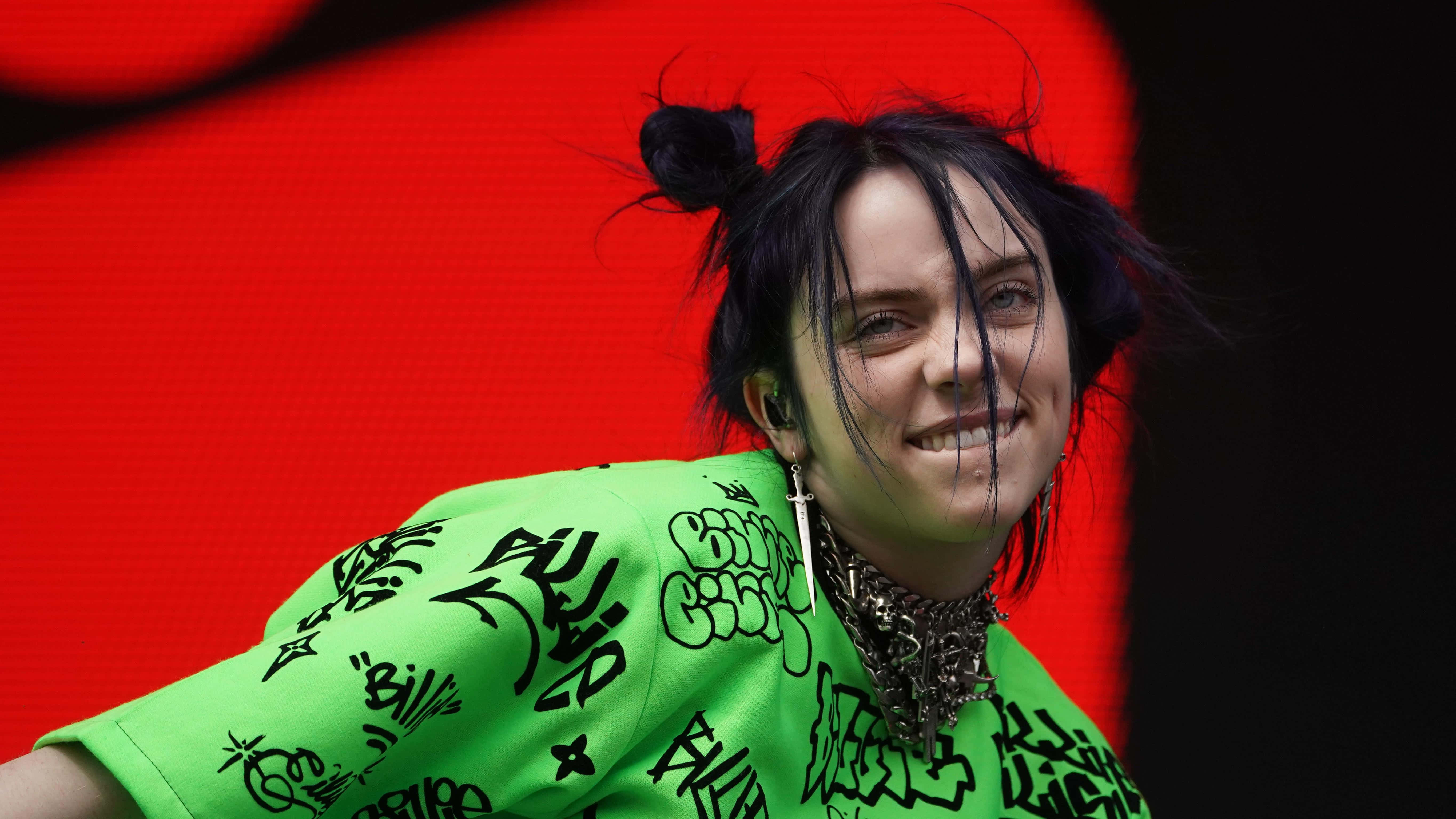 Billie Eilish Laptop 桌布 壁紙 — 比莉·艾利許在鮮紅色背景前穿著螢光綠色塗鴉襯衫，露出燦爛的笑容。