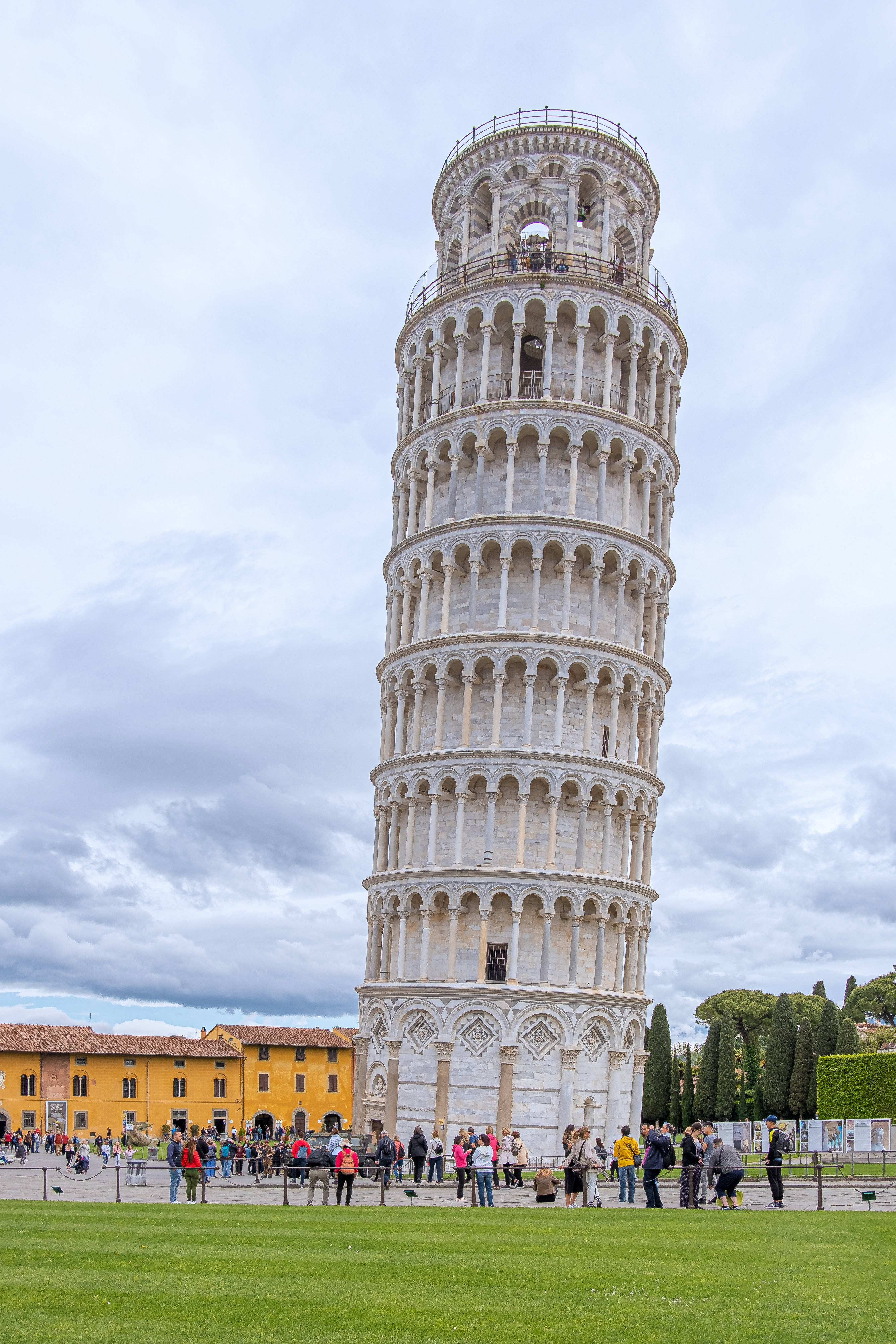 Tuscany 桌布 壁紙 — 比薩斜塔傾斜地矗立在多雲的天空下，遊客聚集在下面的草地上。