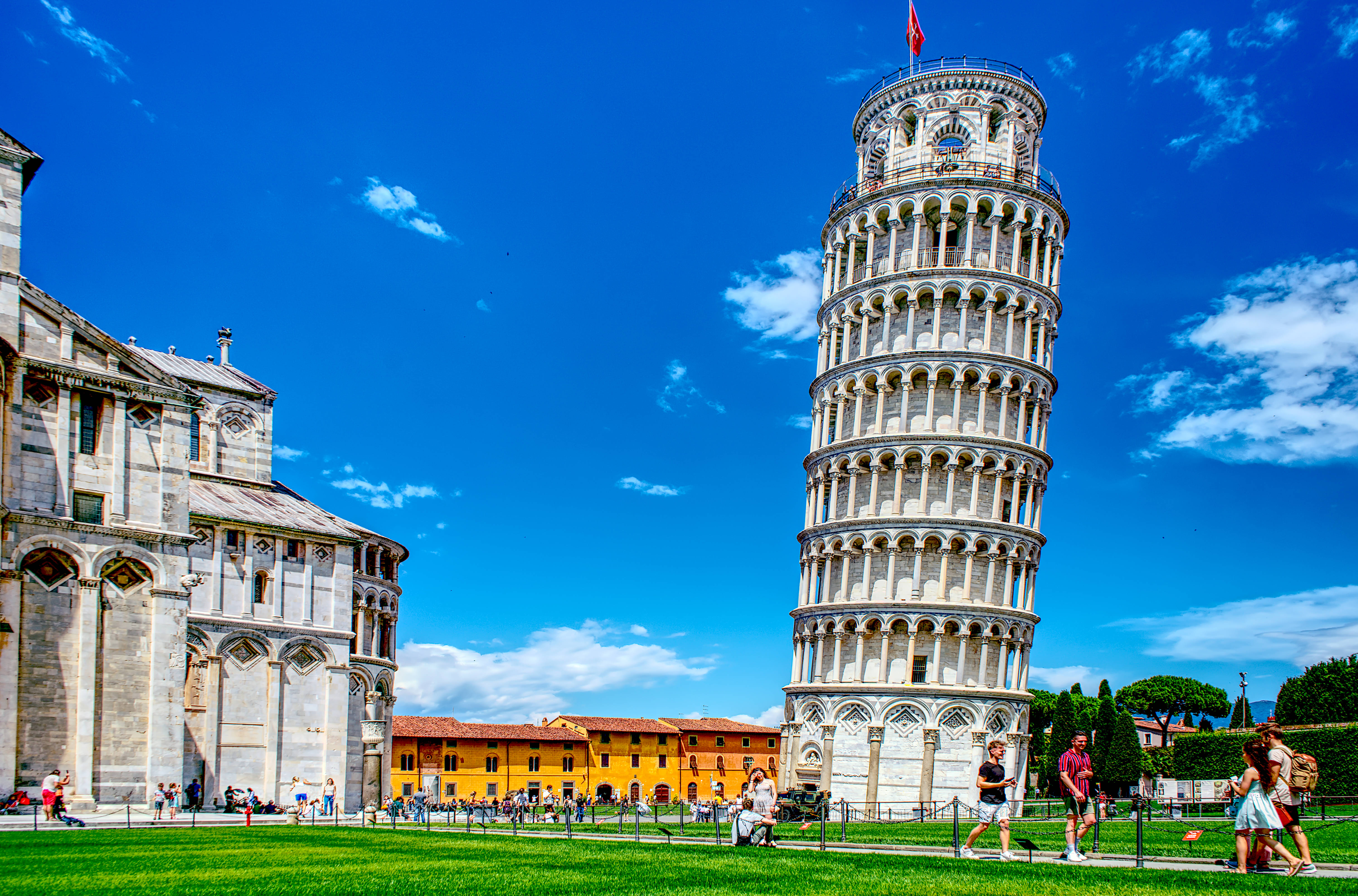 Tuscany 桌布 壁紙 — 比薩斜塔傾斜地矗立在蔚藍的天空下，天空中有散落的雲朵，陽光明媚的日子裡周圍都是遊客。