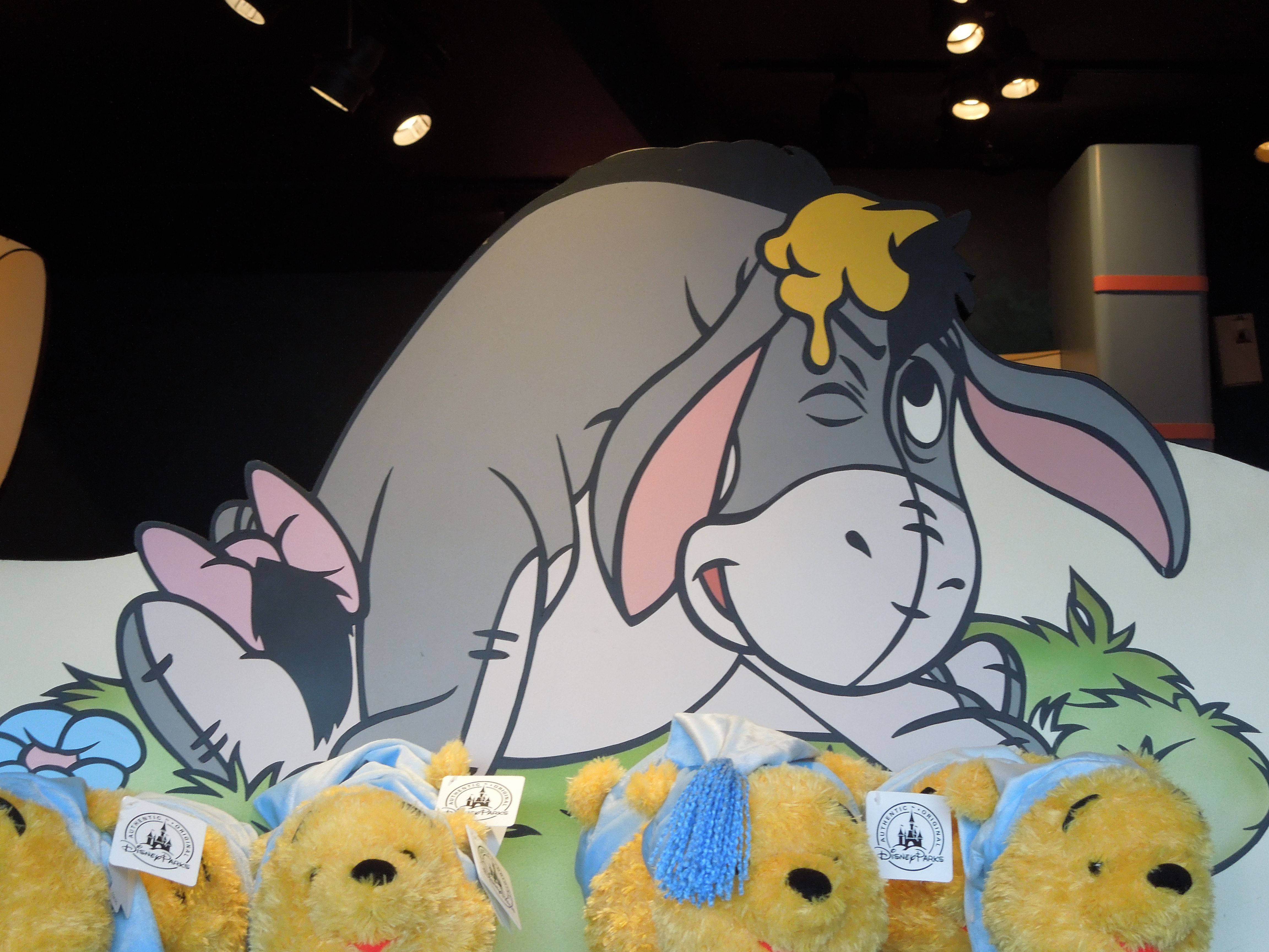 Eeyore 桌布 壁紙 — 毛絨小熊維尼玩具繫著藍色蝴蝶結，坐在昏暗室內展示中一個大型卡通屹耳剪影前。