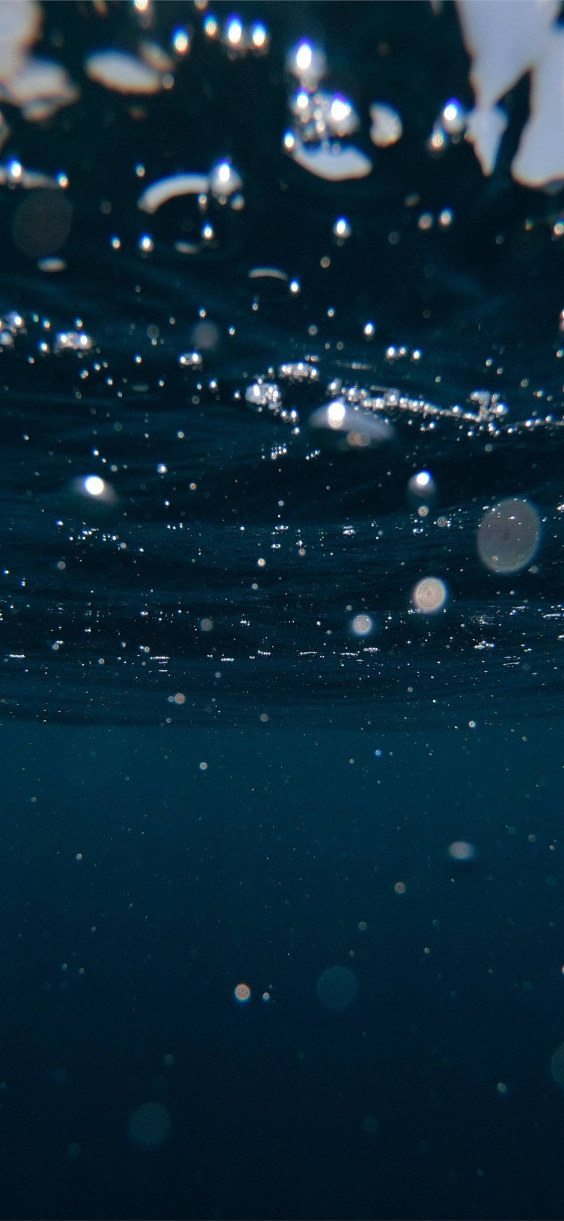 水 桌布 壁紙 — 氣泡穿過深藍色海水上升，陽光在其表面閃爍，營造出寧靜的水下場景。