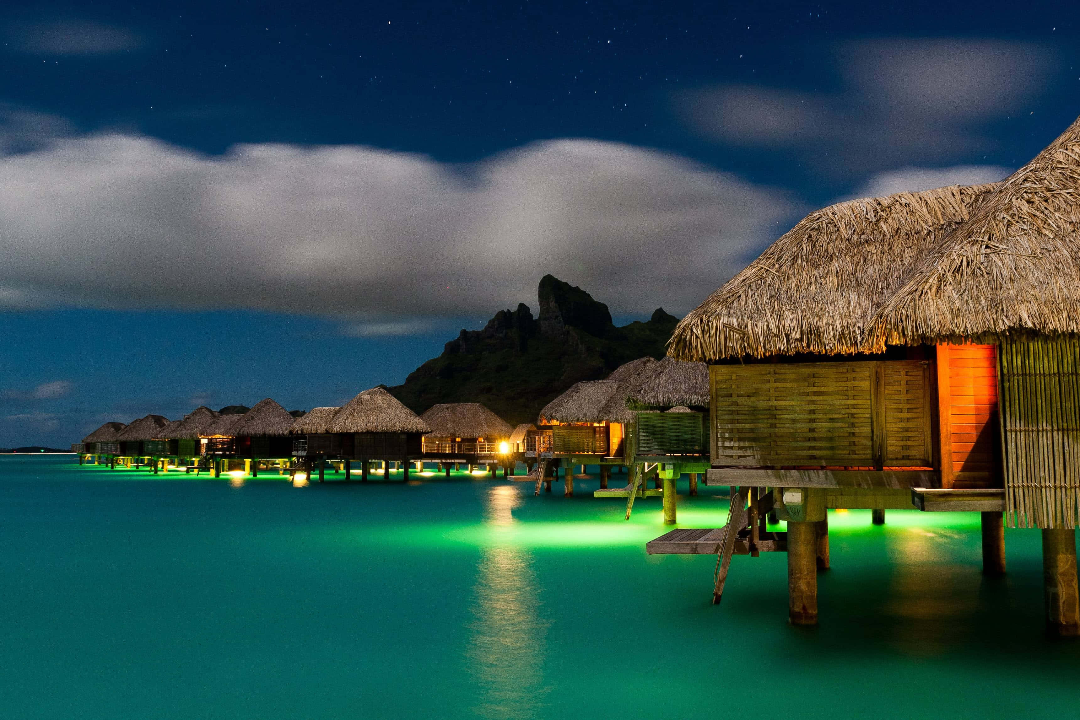 Bora Bora Beach 桌布 壁紙 — 水上平房在星空下溫暖地發光，碧綠色的海水反射著它們的燈光。