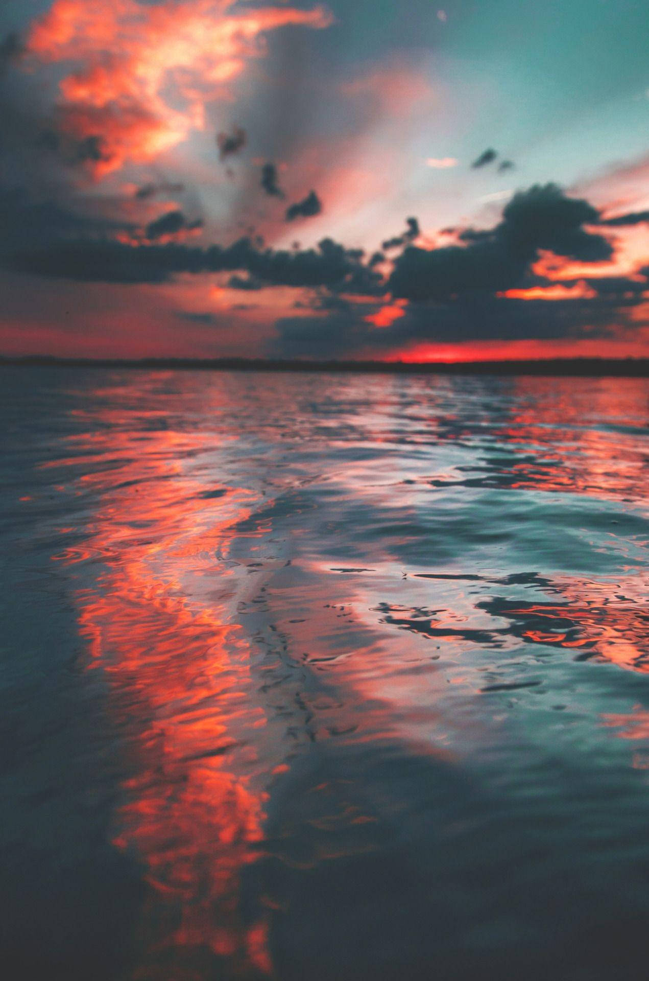 Ocean Sunset 桌布 壁紙 — 水上戲劇性的日落，火橙色雲彩在漣漪波紋中反射，下方是青綠色的天空。