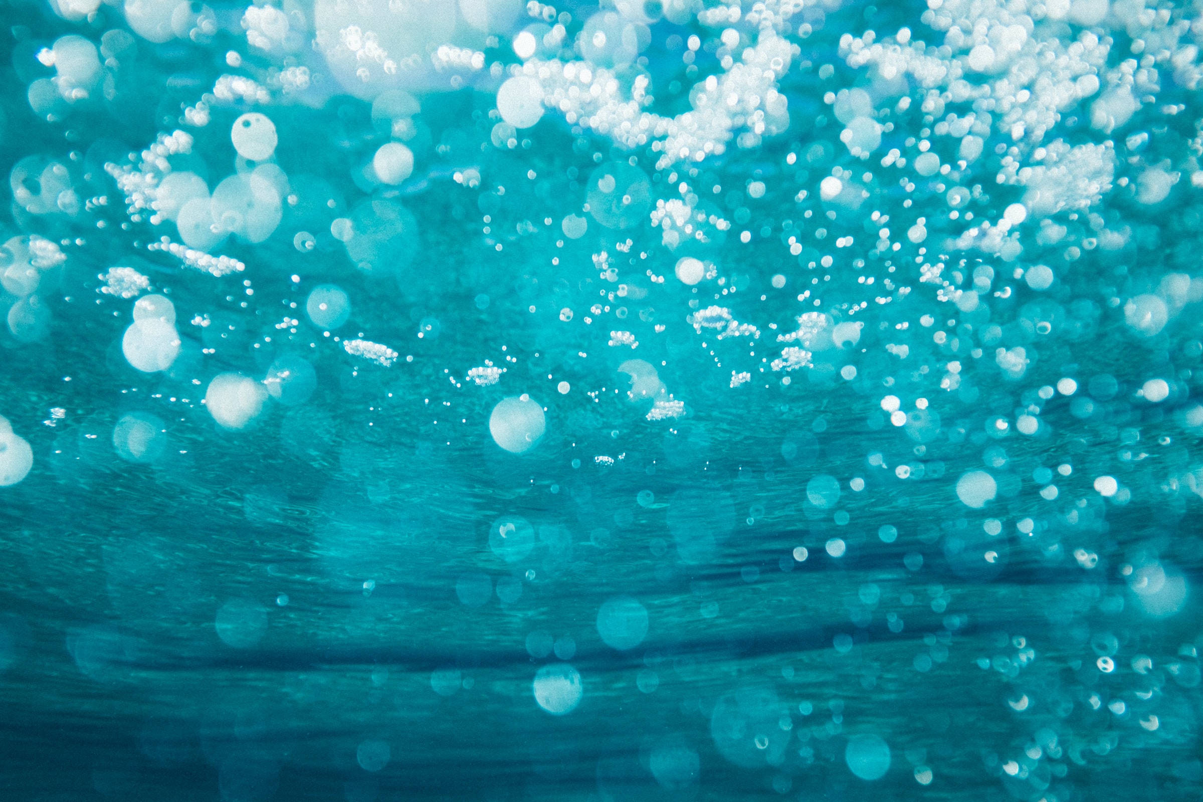海洋藍 桌布 壁紙 — 水下視角，無數閃爍氣泡穿過充滿活力的碧綠海水，帶有柔和散景效果。