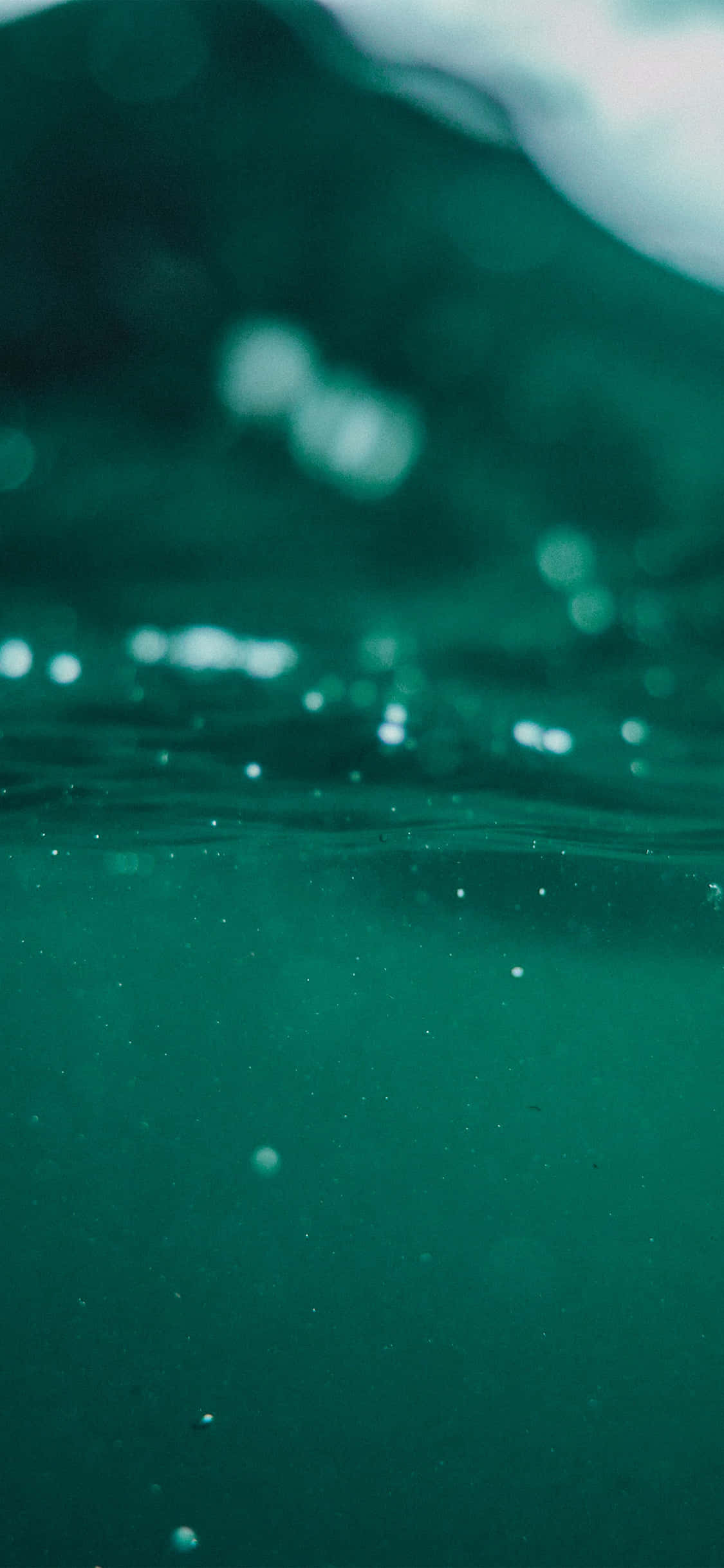 Underwater iPhone 桌布 壁紙 — 水下觀看帶有光折射和氣泡向水面上升的藍綠色水域。
