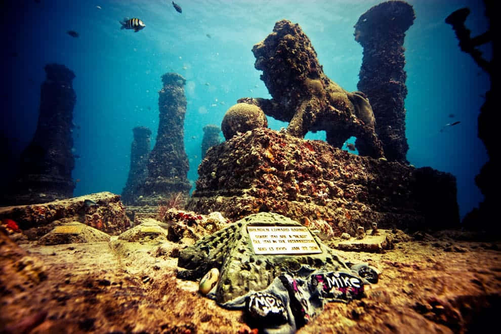 Underwater Scary Ocean 桌布 壁紙 — 水下遺跡，有獅子雕像和魚在藍色海洋深處游動。