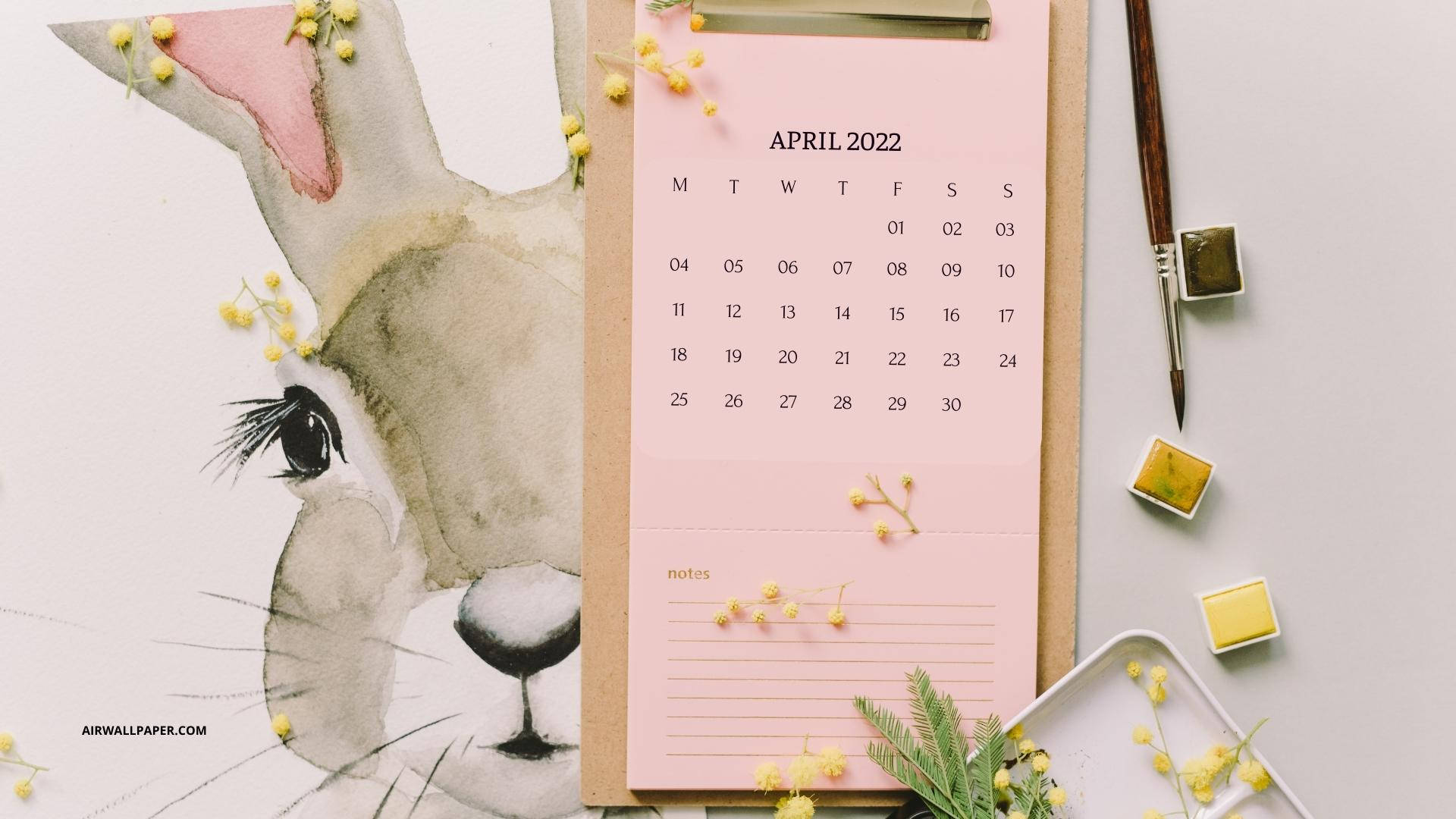 April 桌布 壁紙 — 水彩兔子插圖旁邊是粉紅色2022年4月月曆，有黃色花和美術用品在淺灰色桌上。