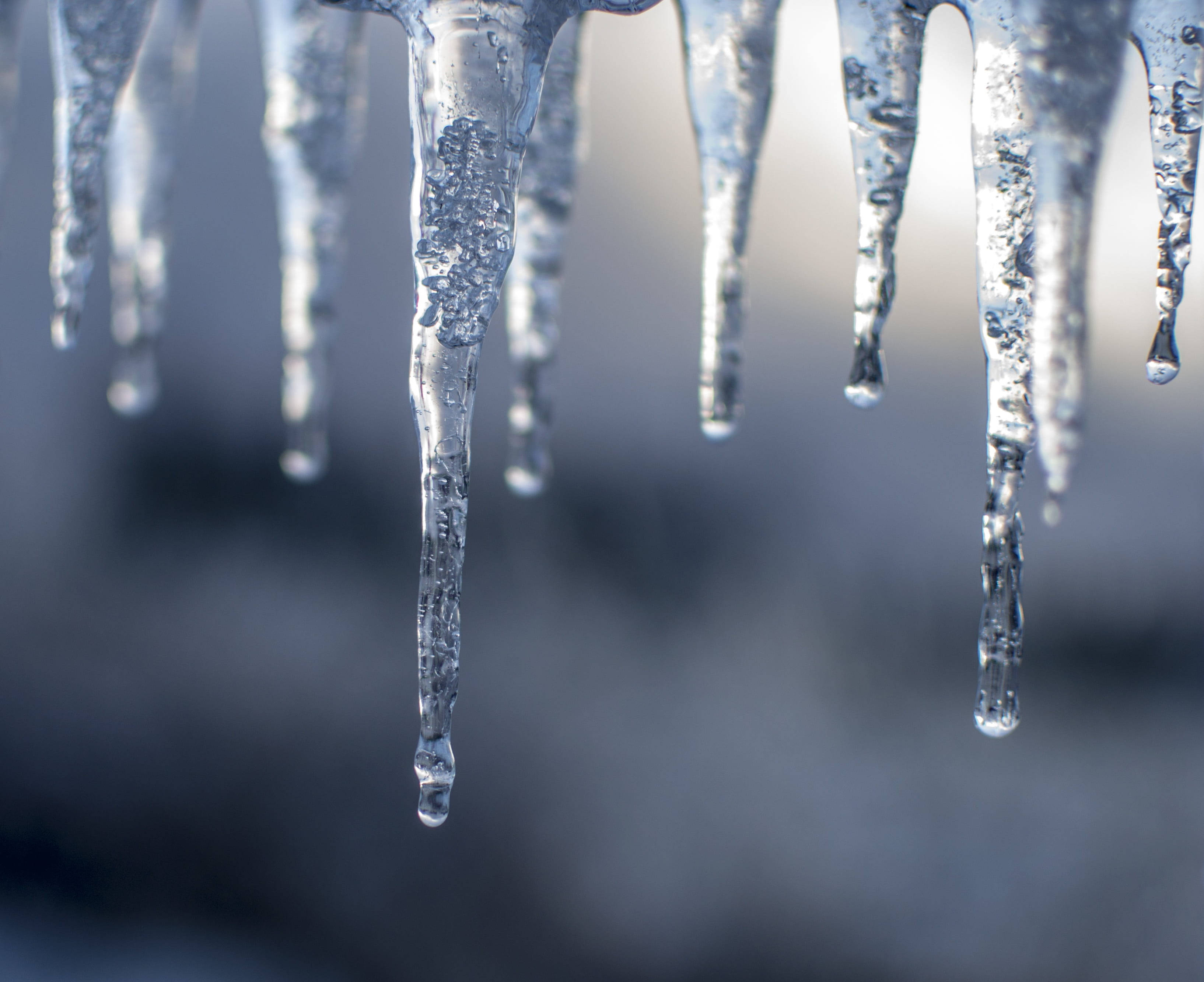 Temperature 桌布 壁紙 — 水晶般清澈的冰柱懸掛在柔和模糊的冬季背景中，光線透過冰體折射。