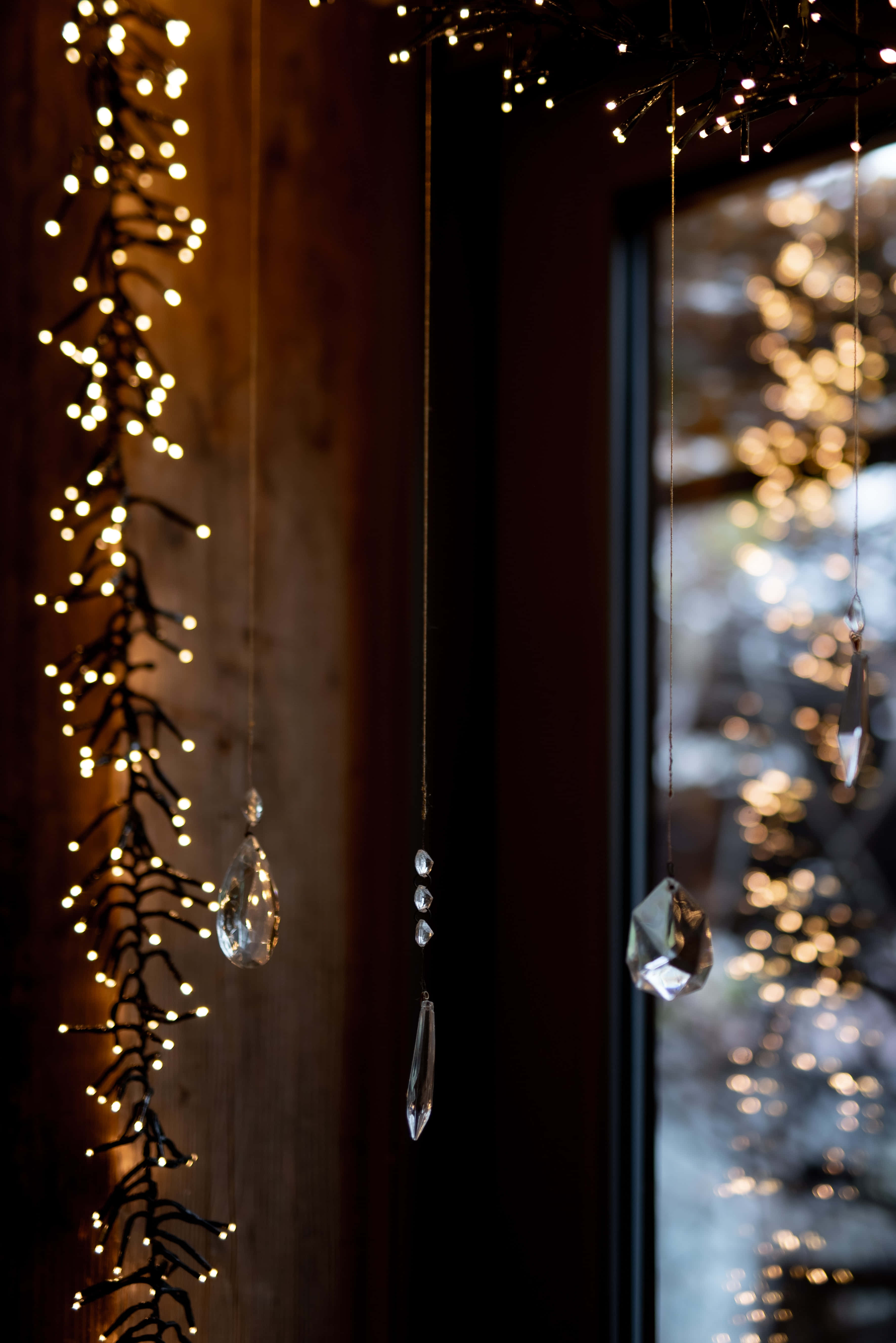 Christmas Light 桌布 壁紙 — 水晶裝飾品掛在窗邊的燈串上，窗外有閃爍的雪樹。