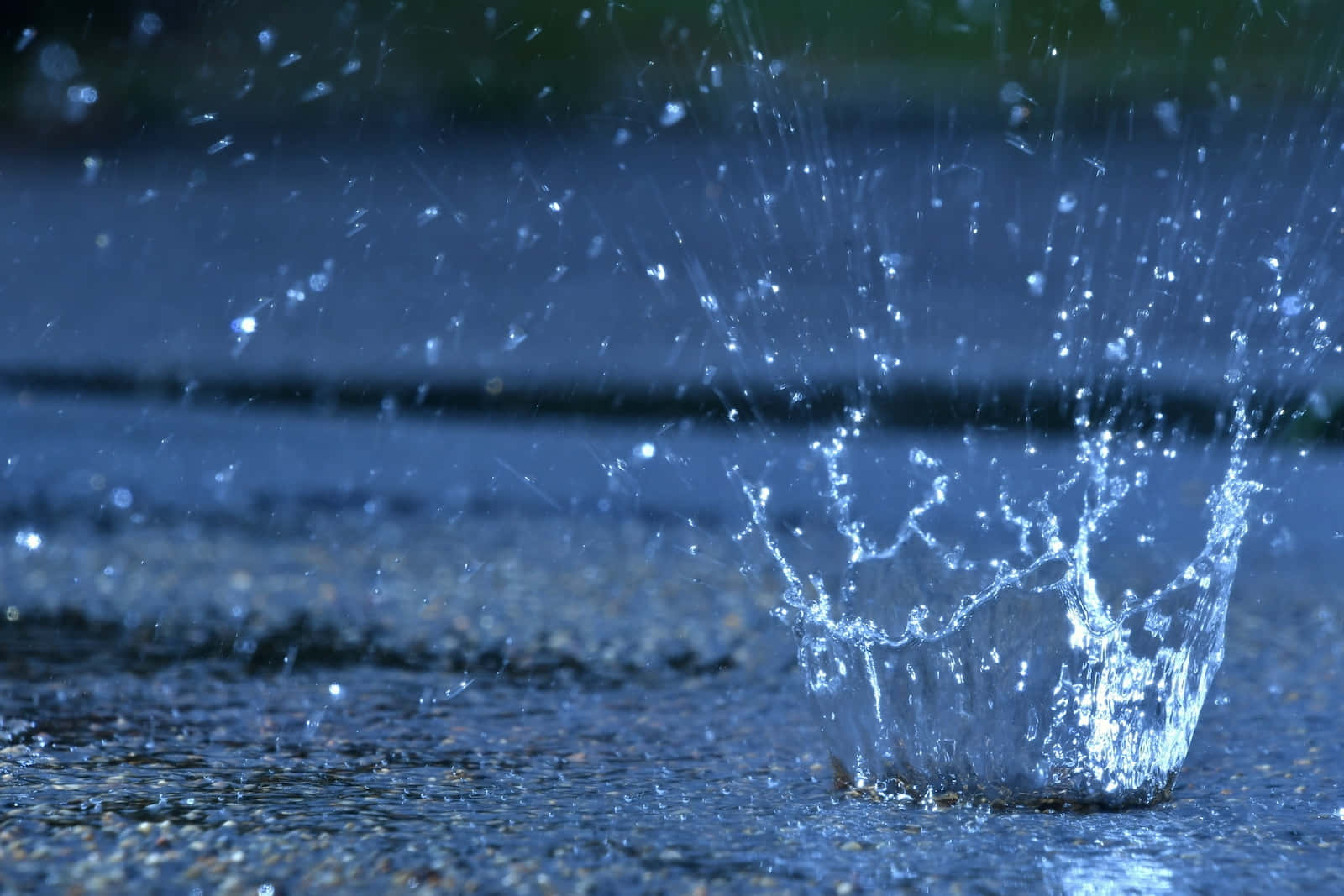 下雨 桌布 壁紙 — 水滴在濕漉漉的人行道上濺起的特寫，在模糊的藍色背景上形成閃閃發光的水滴。