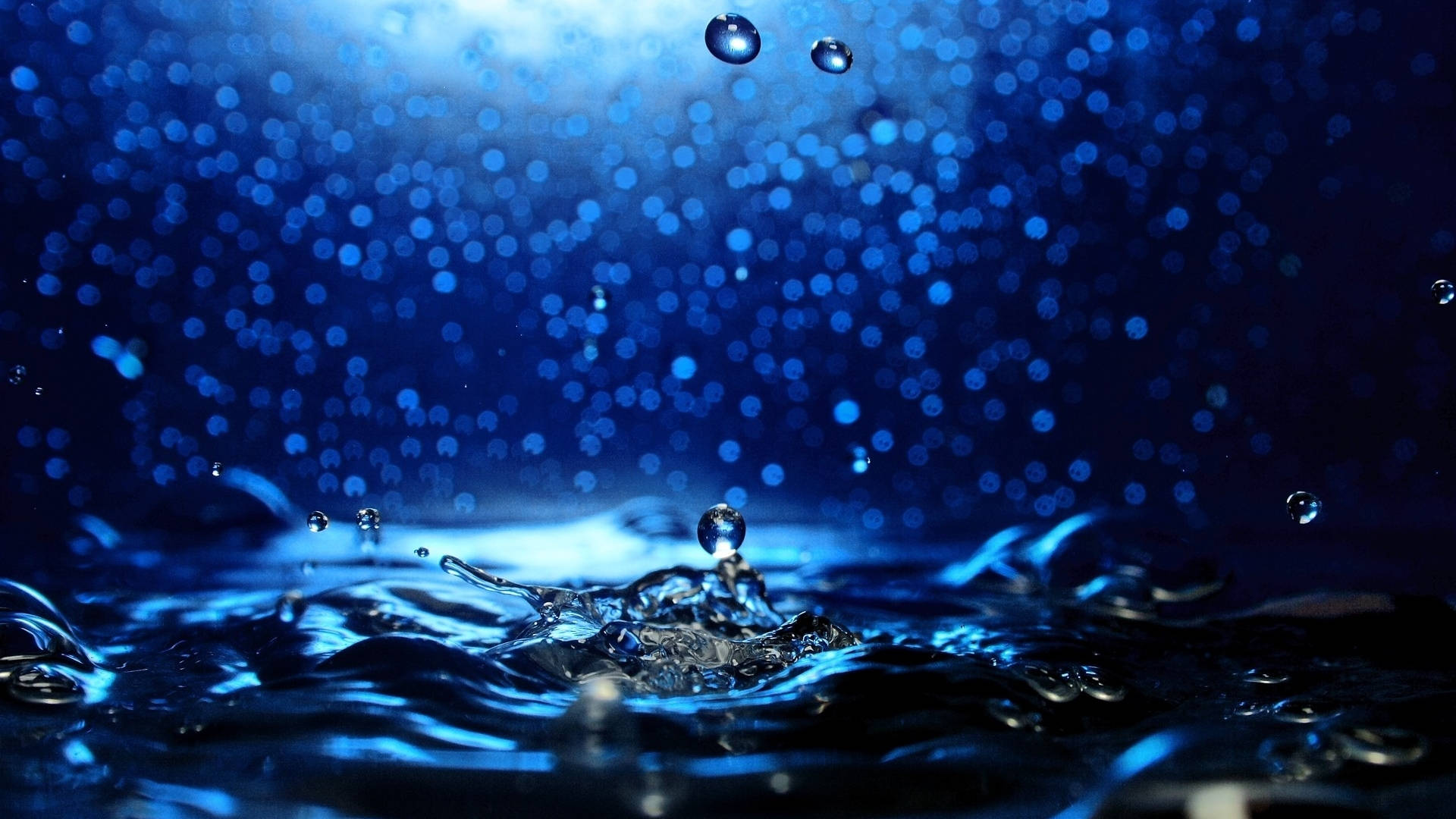 水下動畫 桌布 壁紙 — 水滴懸浮在漣漪藍色表面上空的特寫，背景有散景效果。