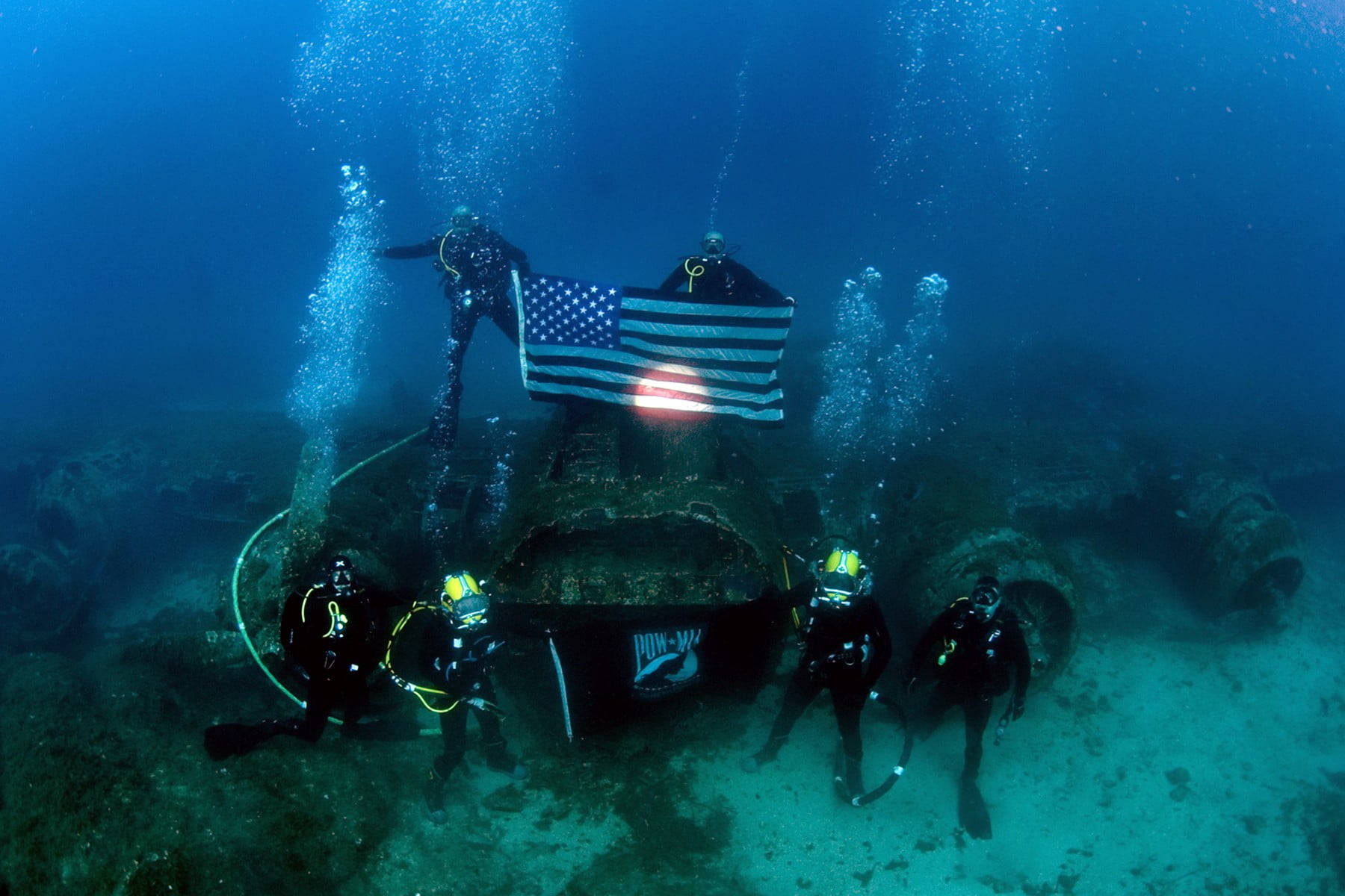 diving 桌布 壁紙 — 水肺潛水員在深藍色海洋中用水底美國國旗向沉船致敬。