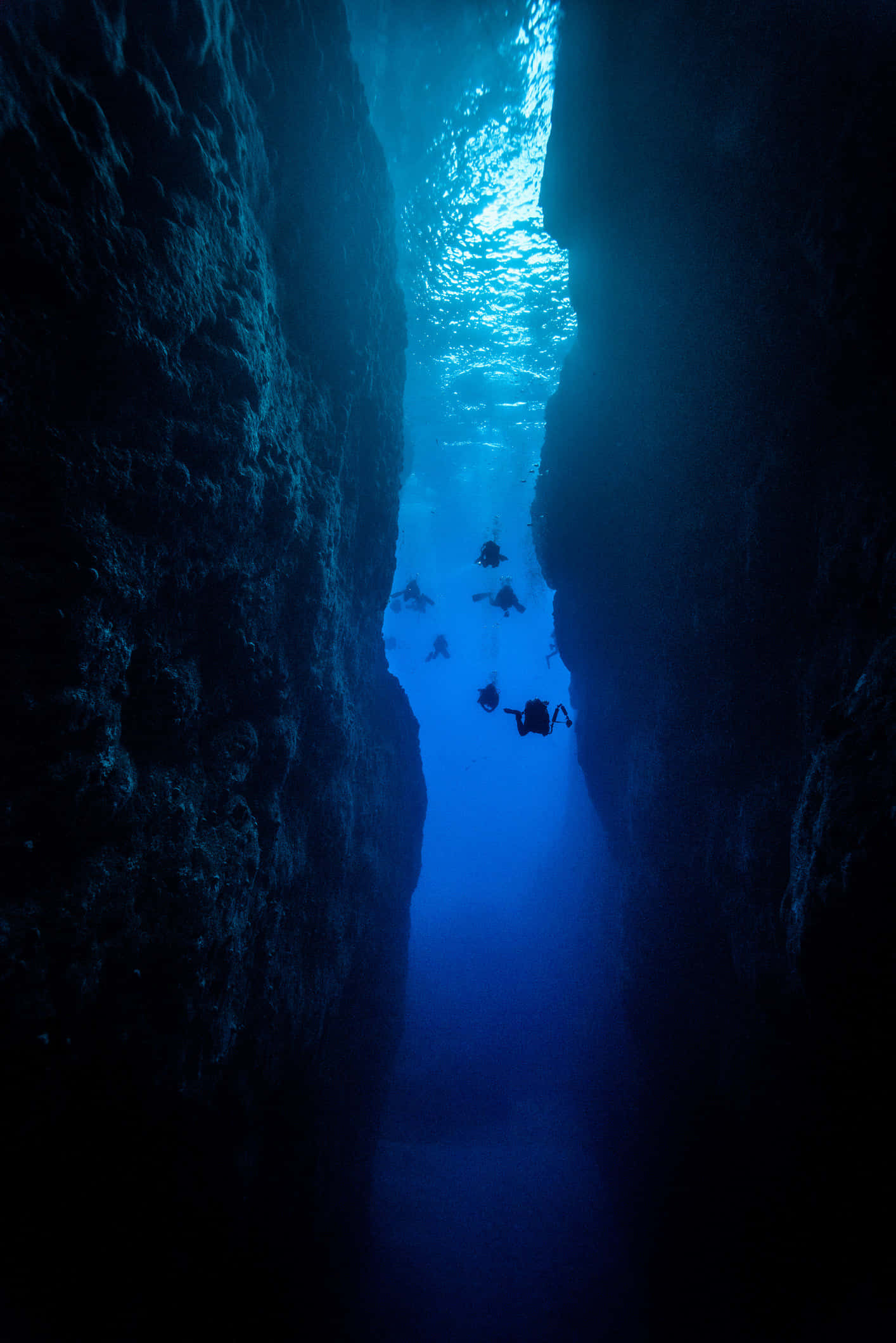 Scary Underwater 桌布 壁紙 — 水肺潛水員探索一個狹窄的水下峽谷，沐浴在從上方過濾下來的藍光中。
