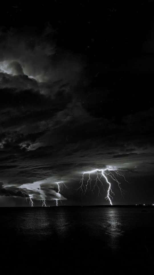 閃電 桌布 壁紙 — 水面上戲劇性的夜空，多道閃電照亮烏雲並在水面反射。