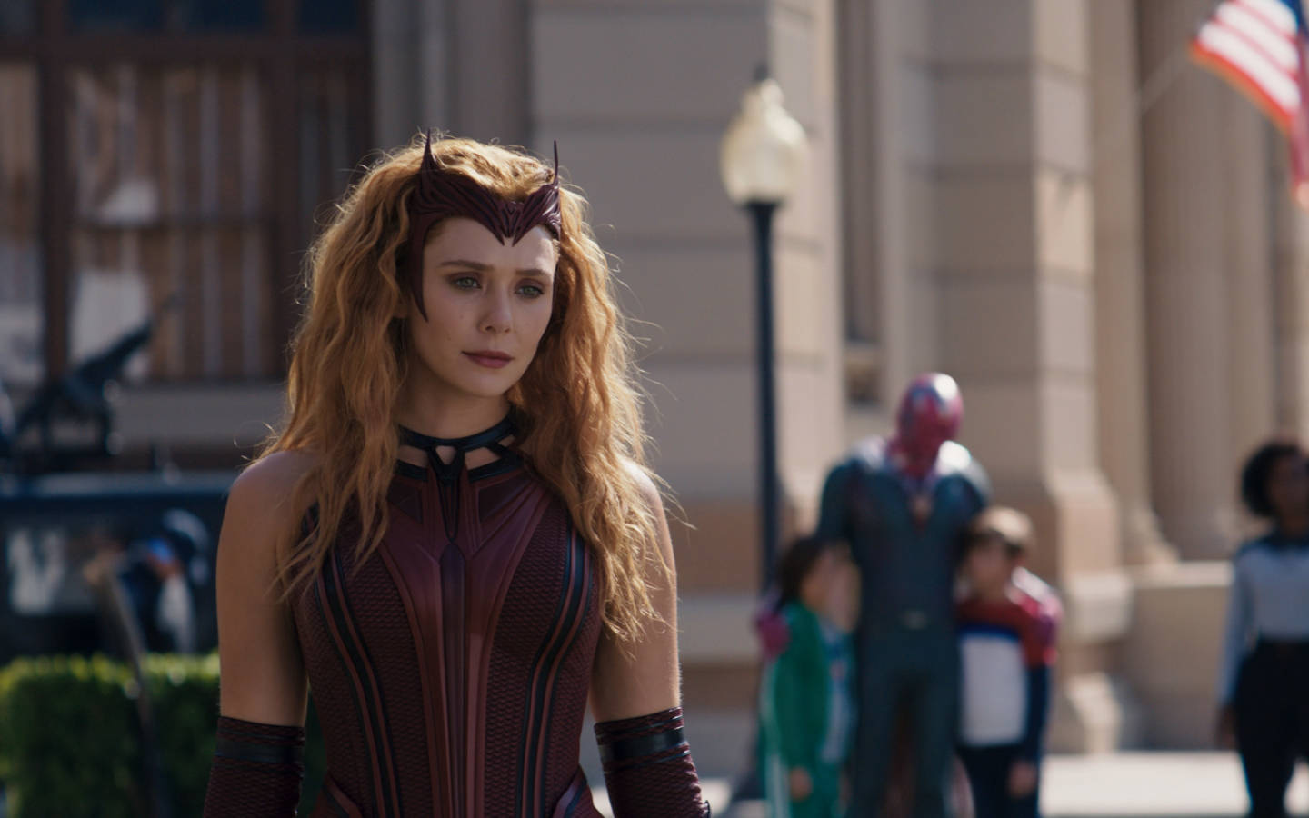 Wanda 桌布 壁紙 — 汪達·馬克希莫夫穿著紅黑女巫服裝，站在陽光明媚的城市街道上，背景有行人和超級英雄。