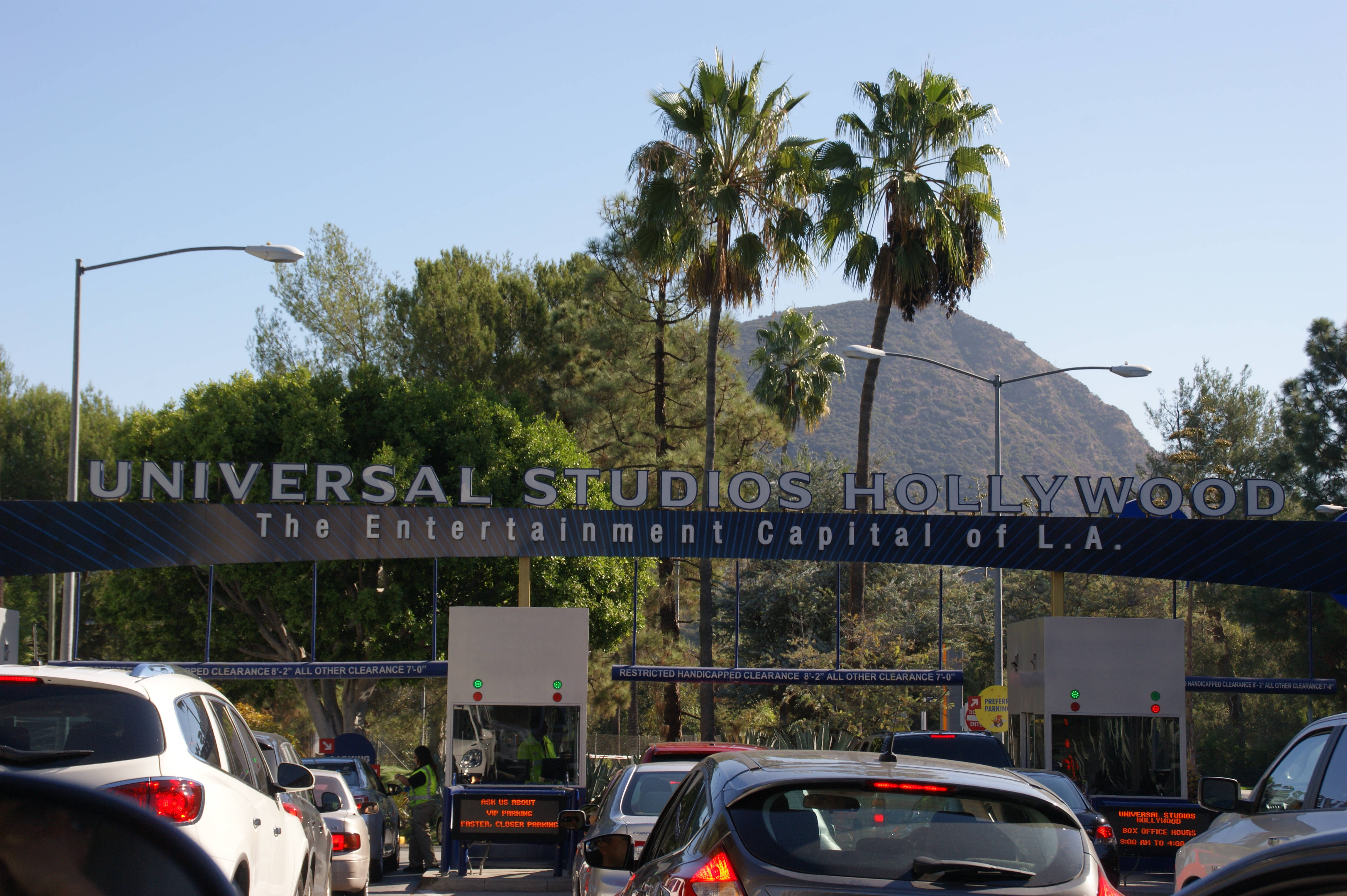 Universal 桌布 壁紙 — 汽車在環球影城好萊塢標誌下排隊，背景有棕櫚樹和陽光照耀的山丘。